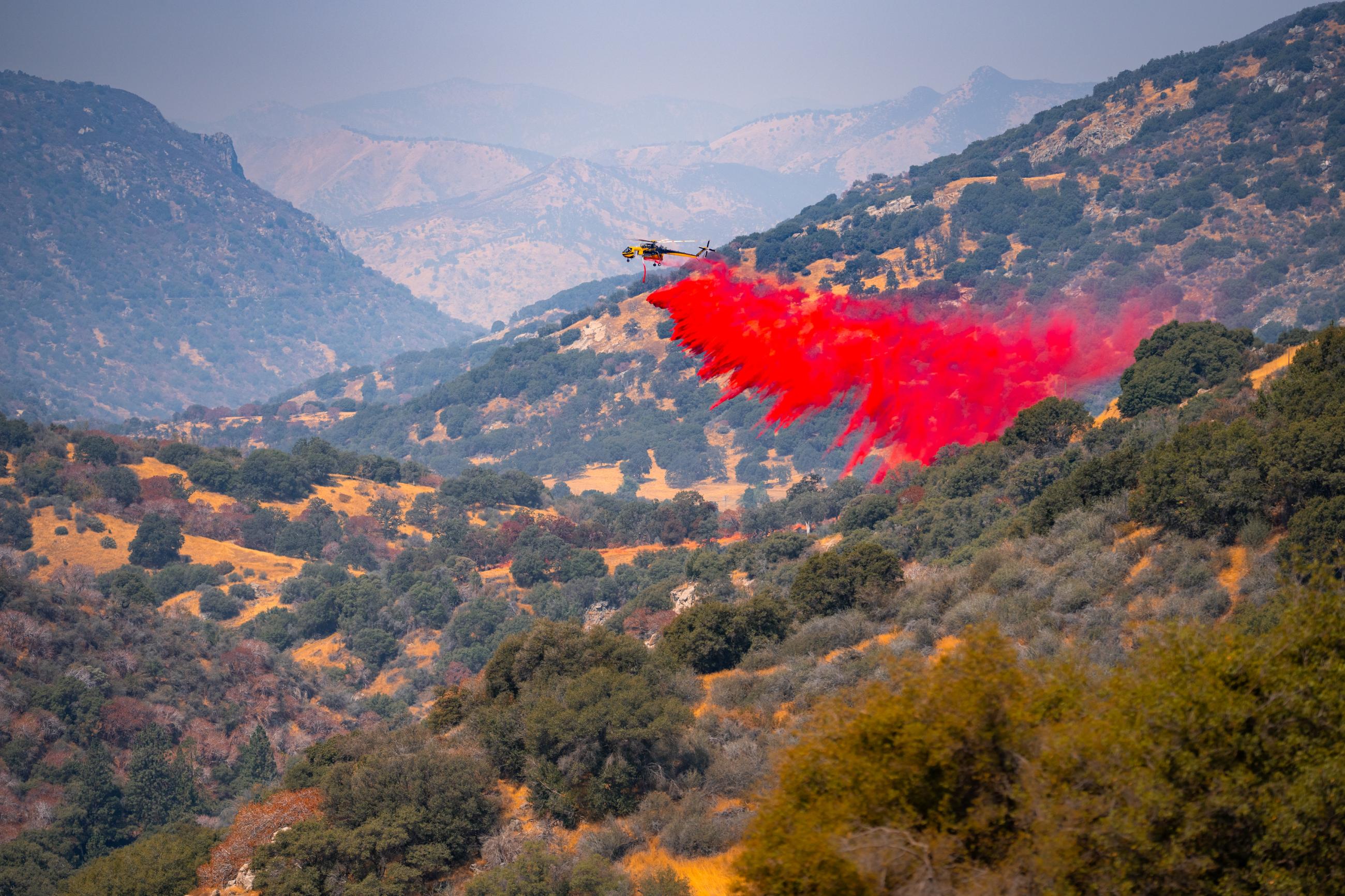 A helicopter dropping fire retardant over vegetation.