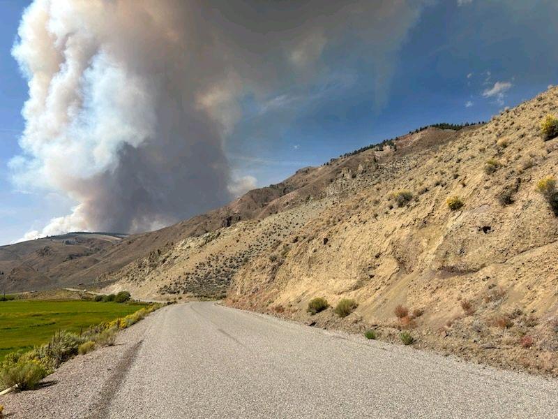 Photo of smoke along a grassy hill with a road running through the middle