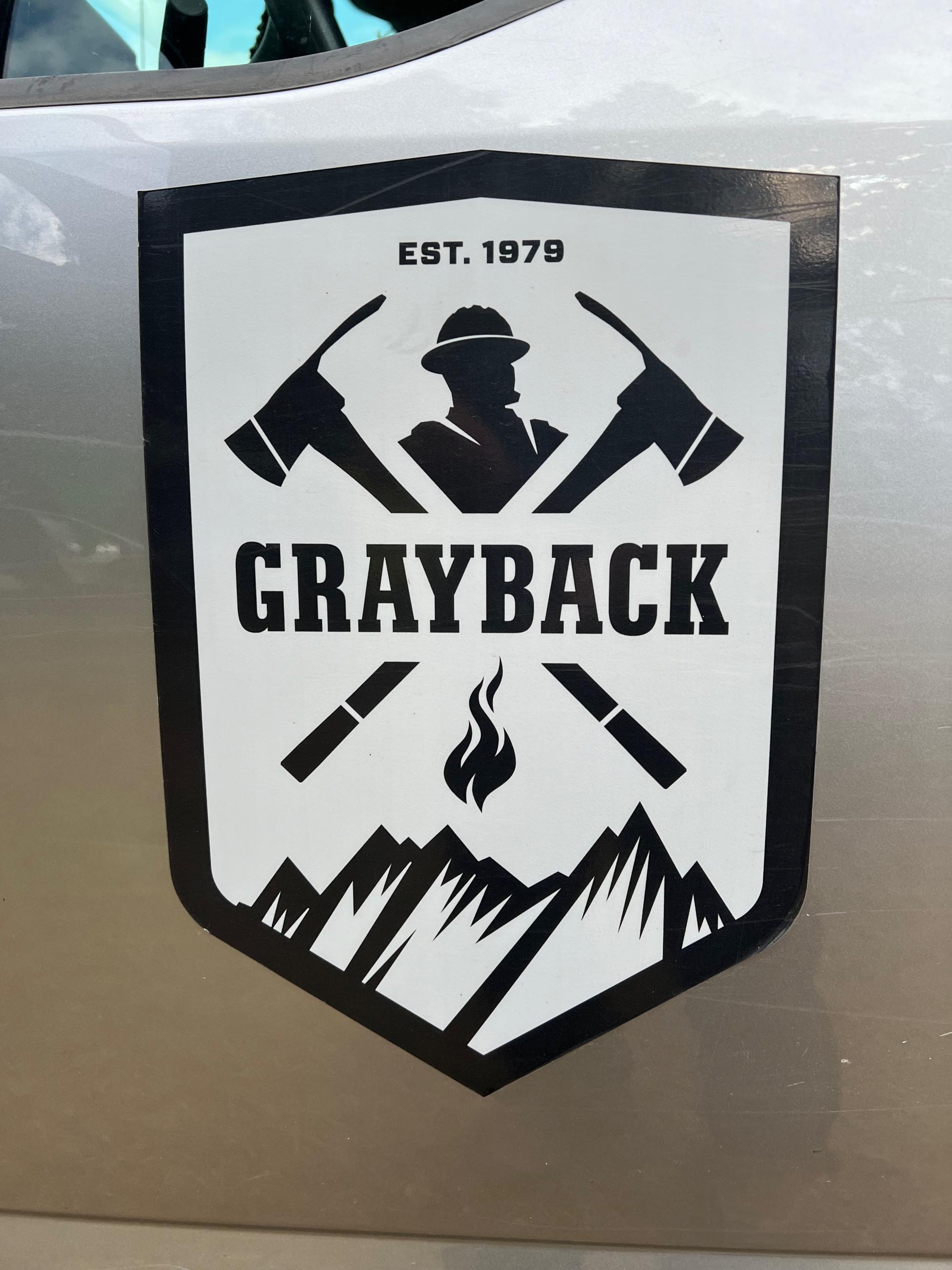 Two crossed axes, a firefighter and mountains are shown on the Grayback Forestry logo