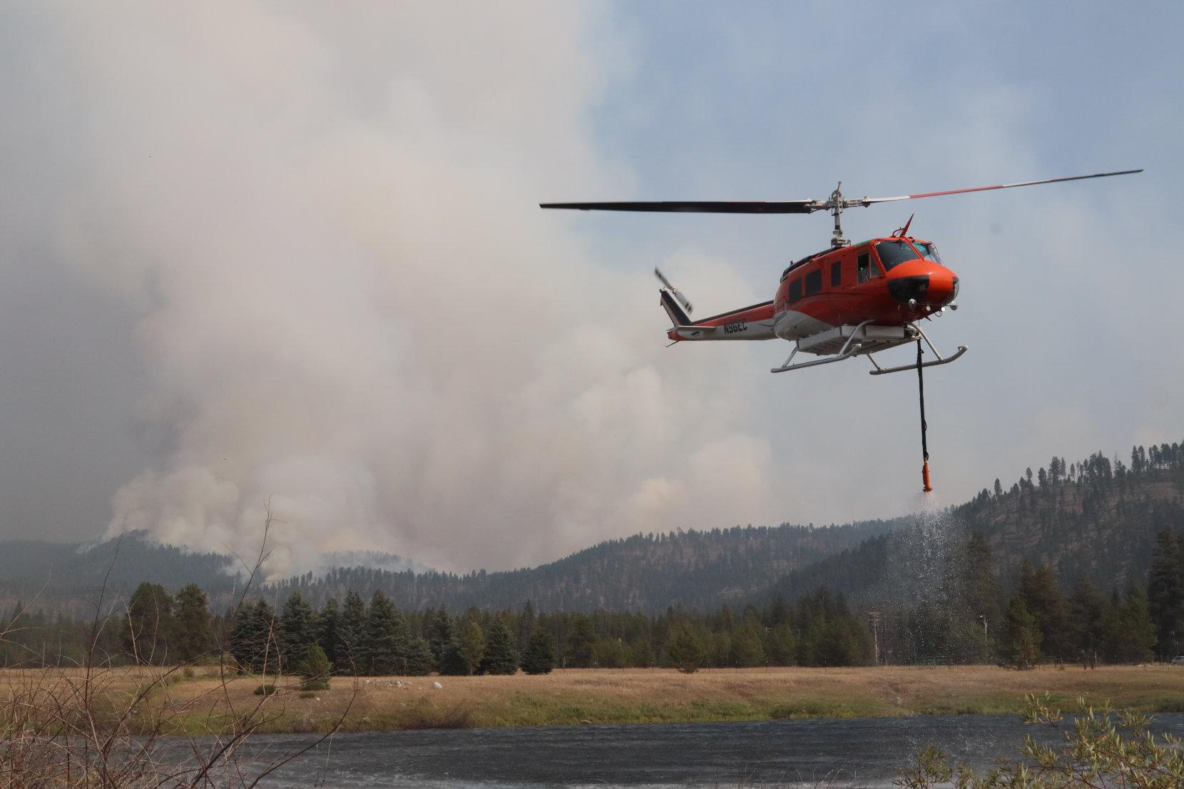 Helicopter Lifts off from Pond with Fire Column in Background