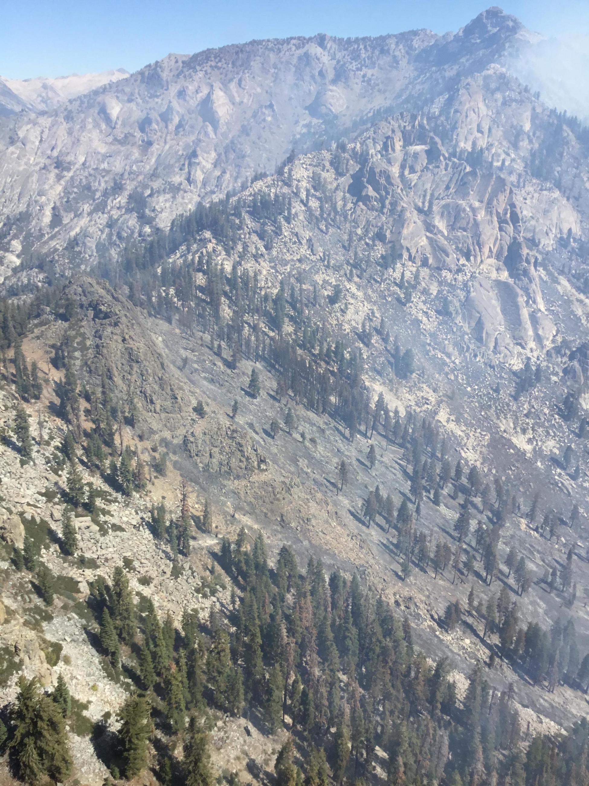 Happy Fire From the Air aerial light blue sky with whispy smoke above a rocky cliff. 