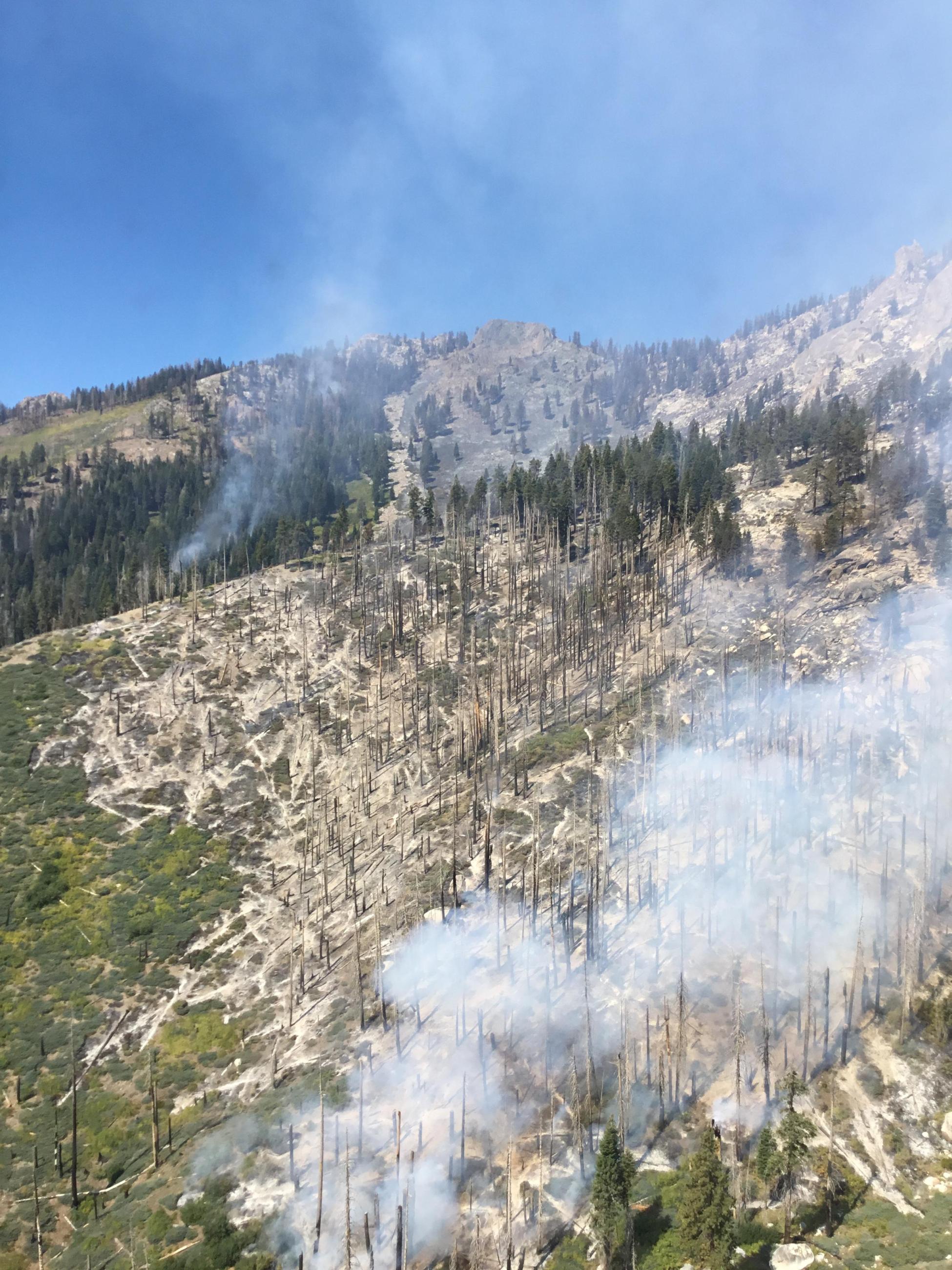 Smoke coming from rocky, steep terrain within the Happy Fire