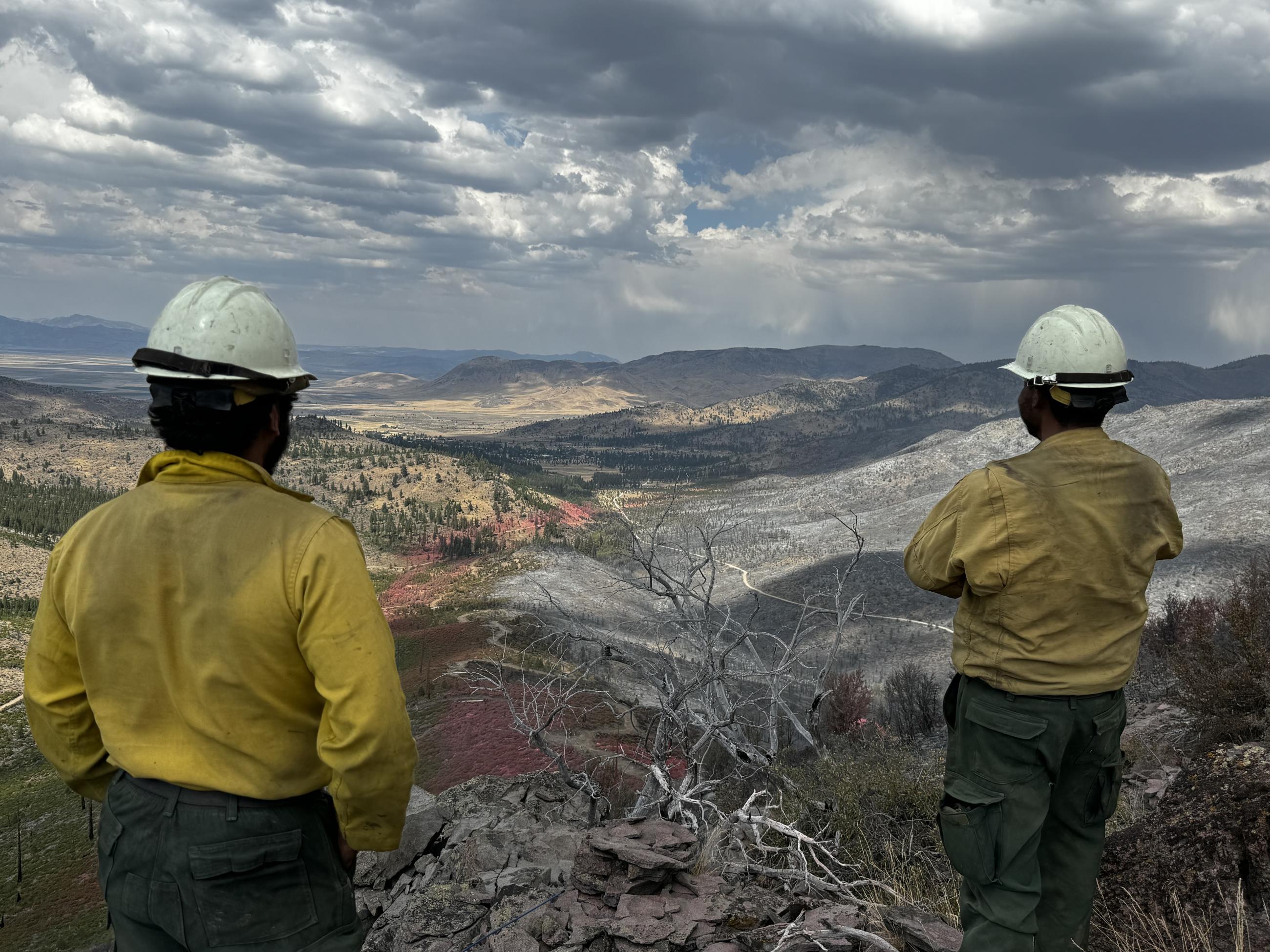 two fire crew members look over a valley that has burned areas