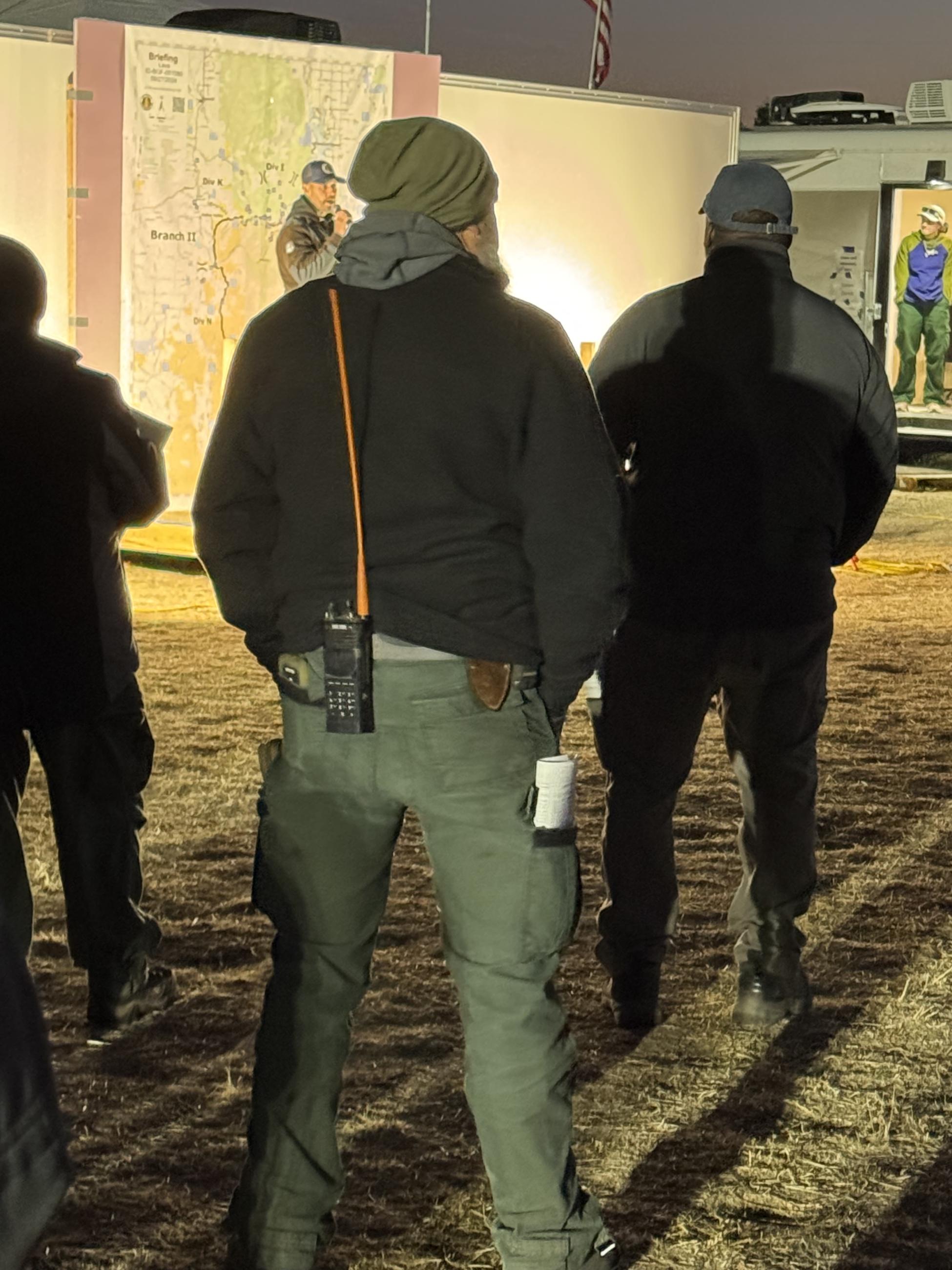 People watching a man present the morning briefing in front of a large Lava Fire map