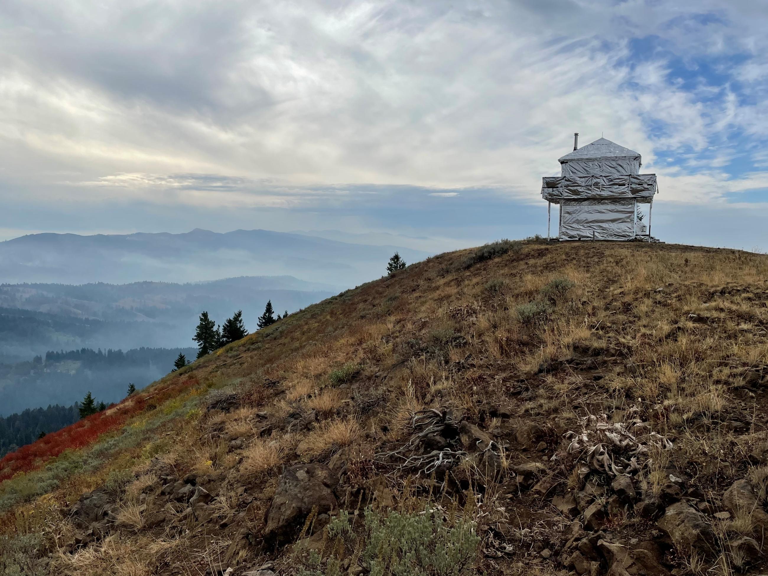 A fire lookout on a ridge wrapped in shiny aluminum foil to protect from fire.