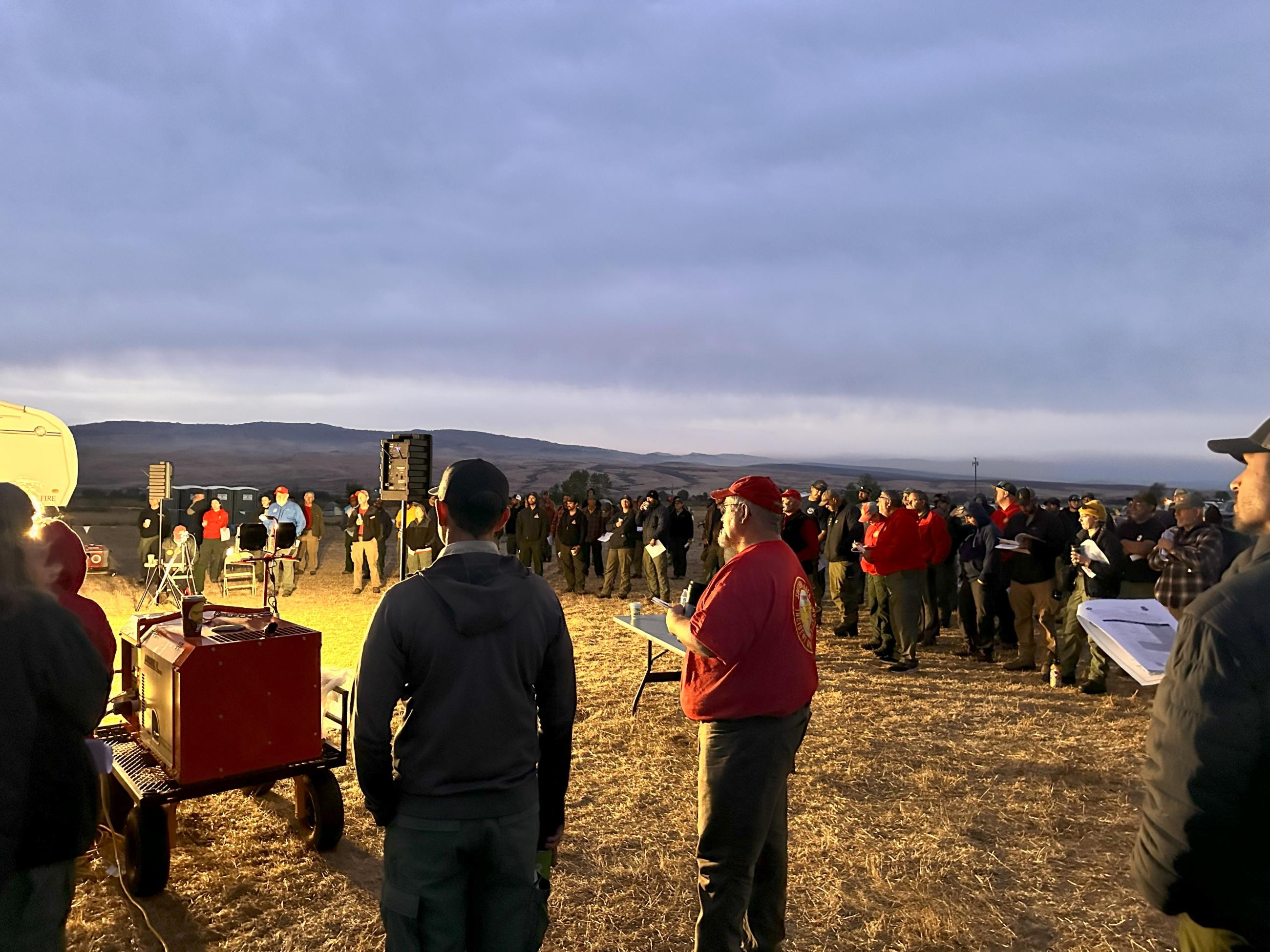 A group of fire personnel stands listening to morning briefing. 