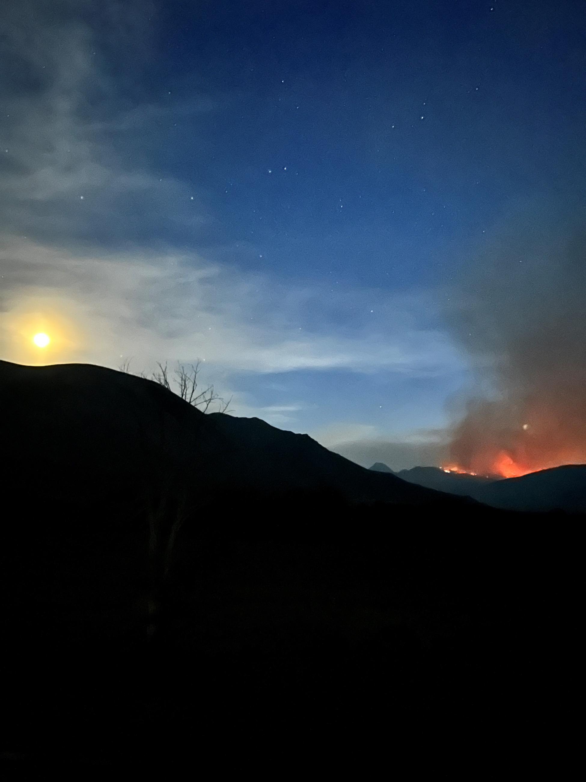 an orange glow above a dark mountain with stars in the sky