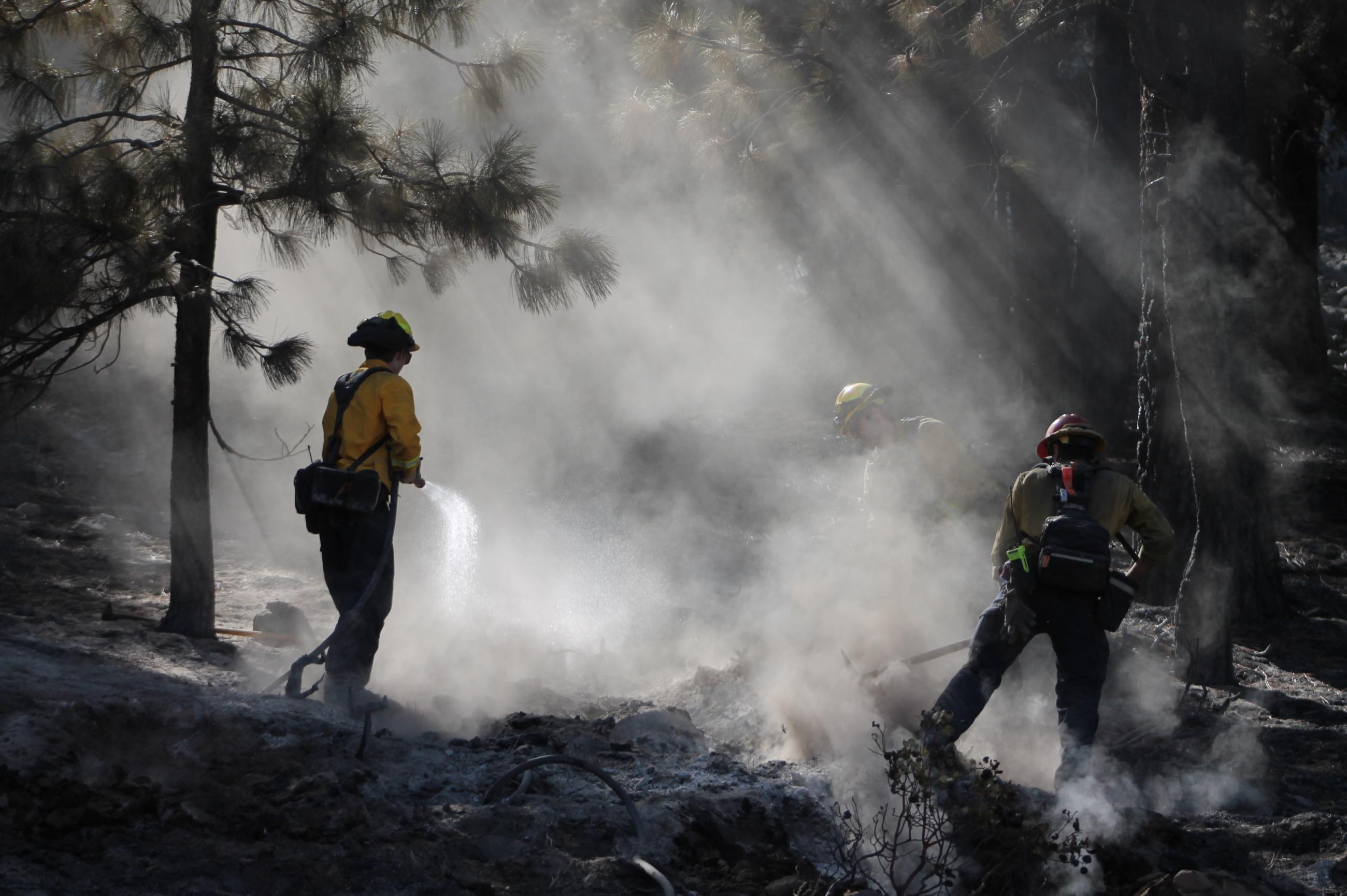 Photo showing three firefighters mopping up, one is spraying water and two are using tools to dig.