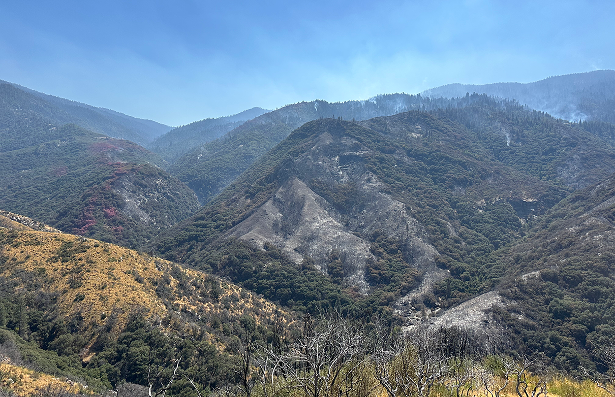 Small wisps of smoke drift up from forested mountain tops.