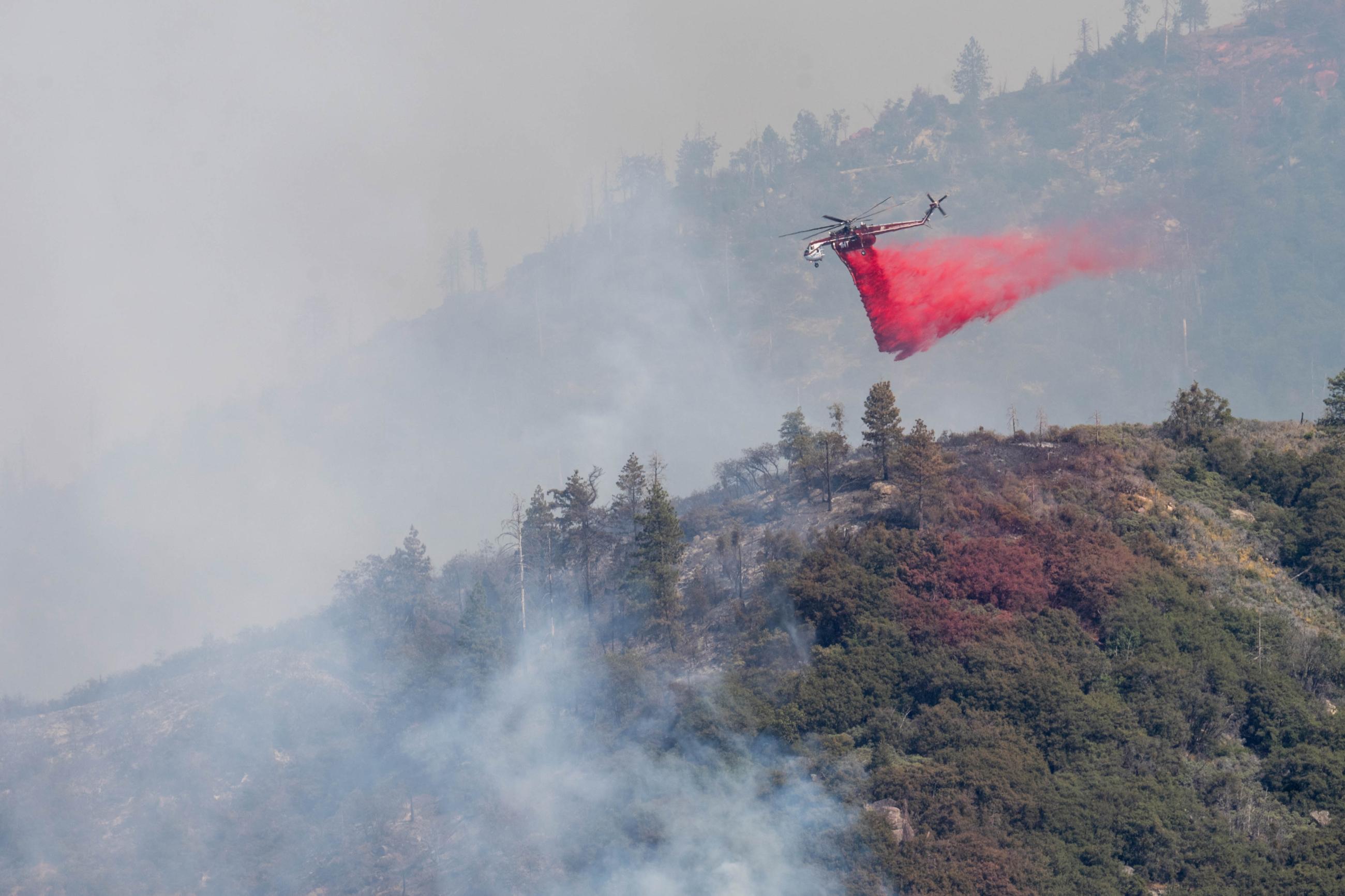 A helicopter drops red liquid along a smokey ridgeline.