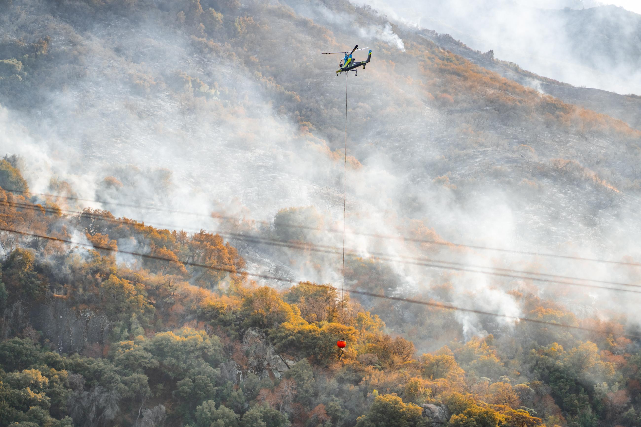 A helicopter flies over a smoky mountainside.