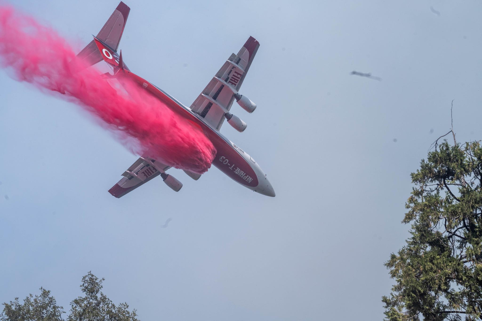 Looking up at the belly of a plane as it drops a pink fire retardant 