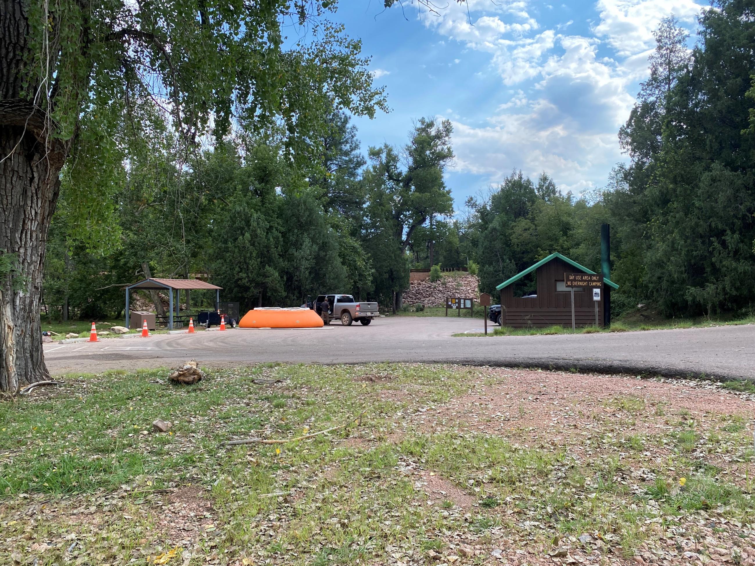 Image shows parking lot with water tank in the woods and structures.
