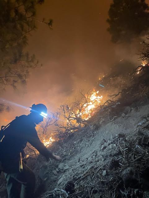 Photo of firefighter climbing steep slope at night with fire in background.