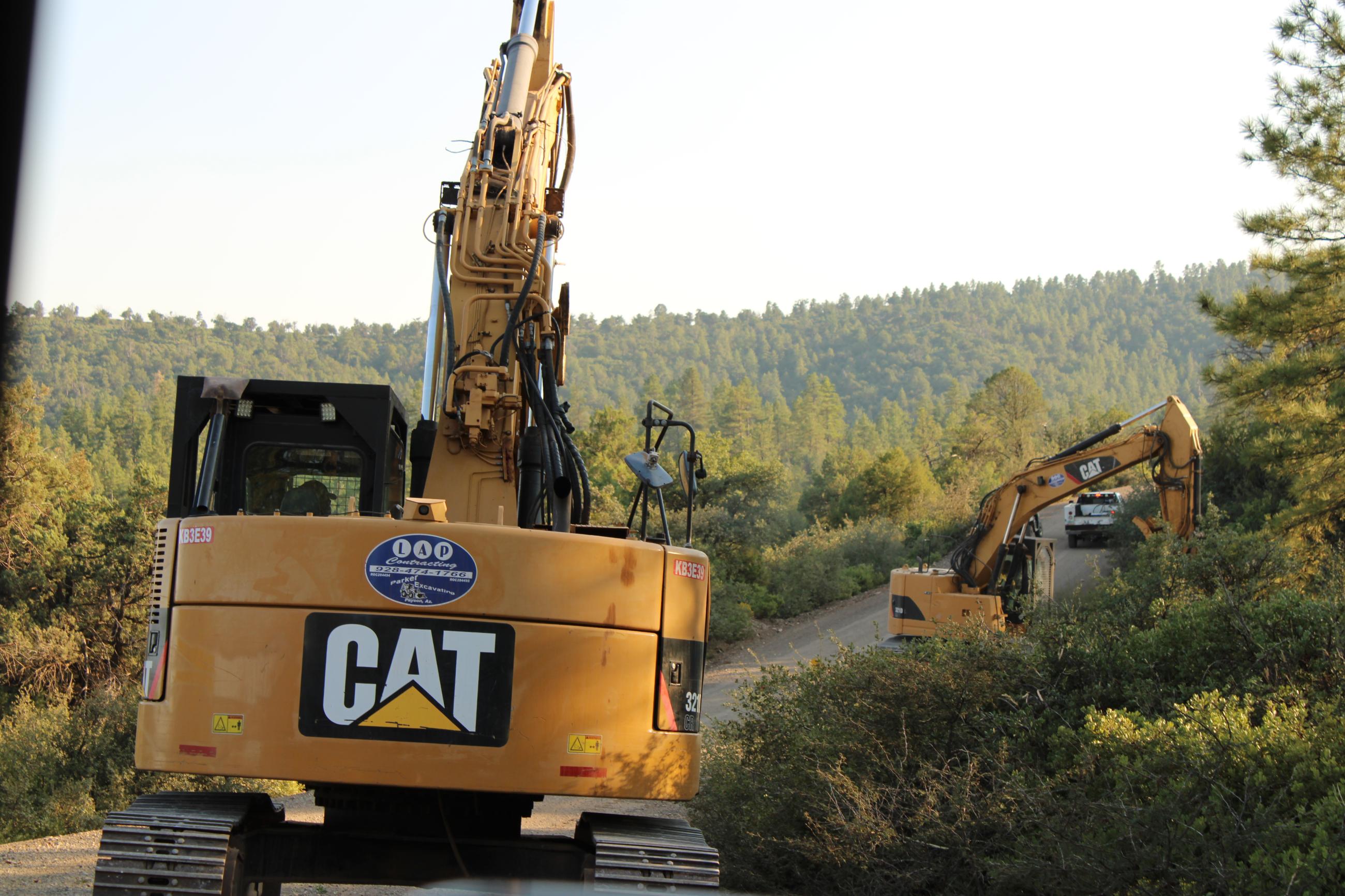Backhoe and heavy equipment works along a wooded road.