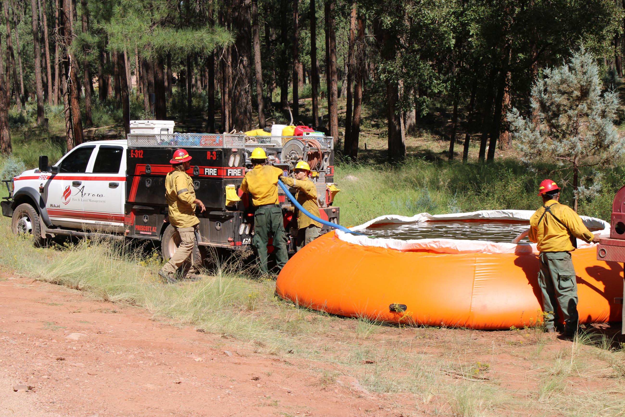 Image of small fire engine refilling with hoses from a tank of water in the woods.