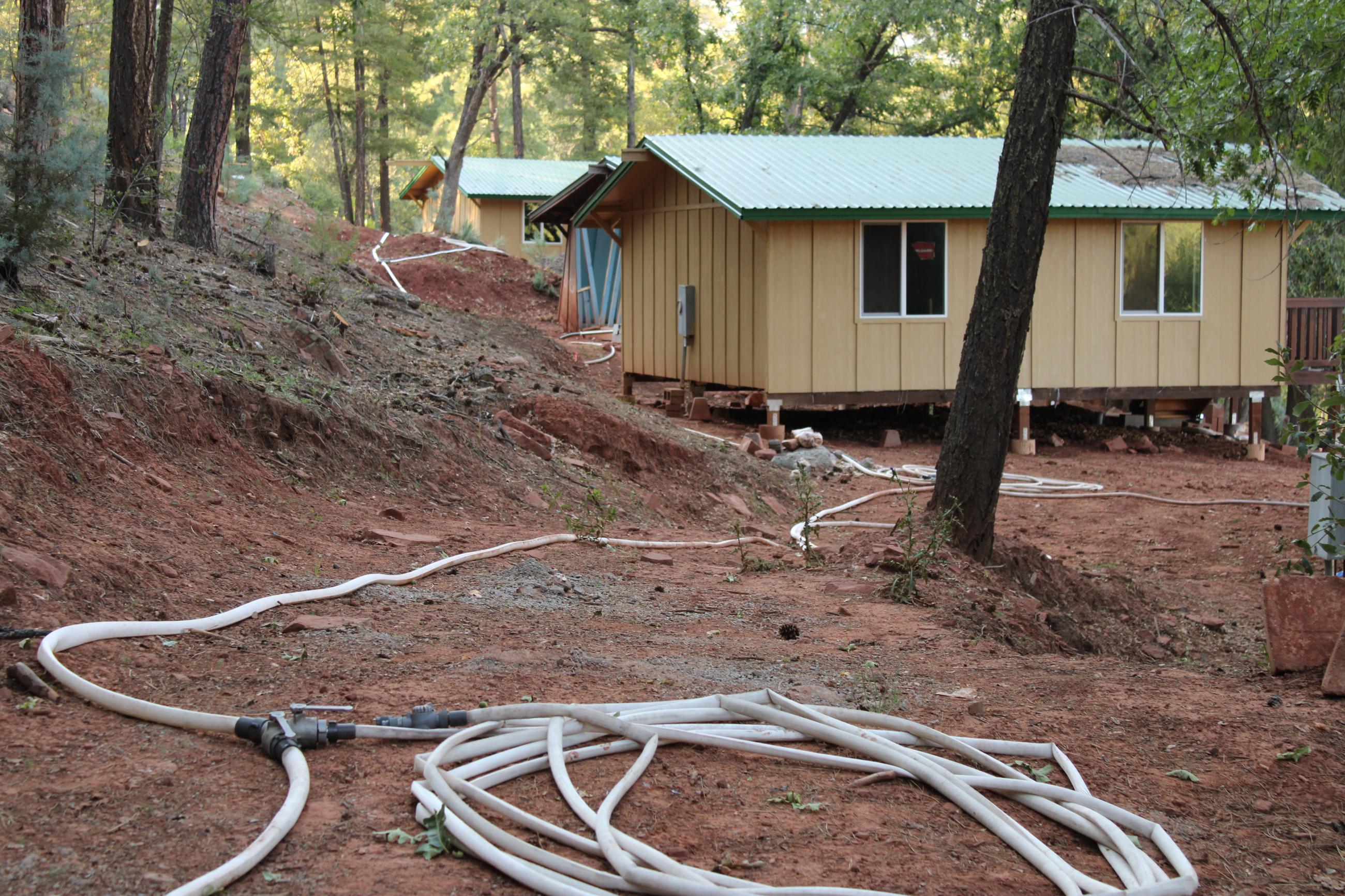 Image of hose coiled on the ground in a forested area with a cabin in the background.