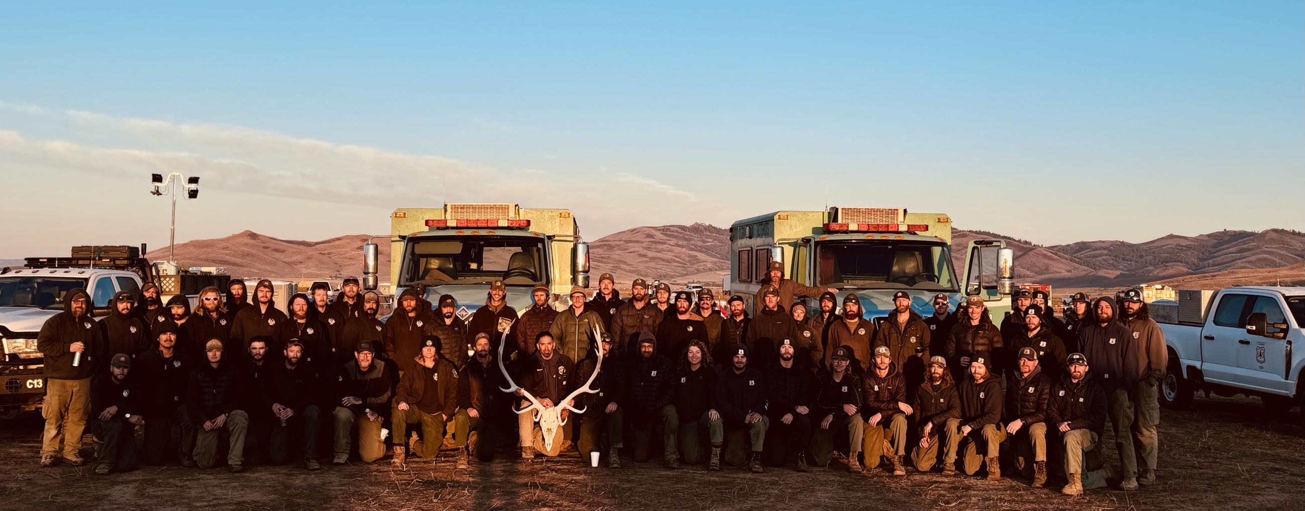 Hotshot firefighters in front of engines with sunset in background.