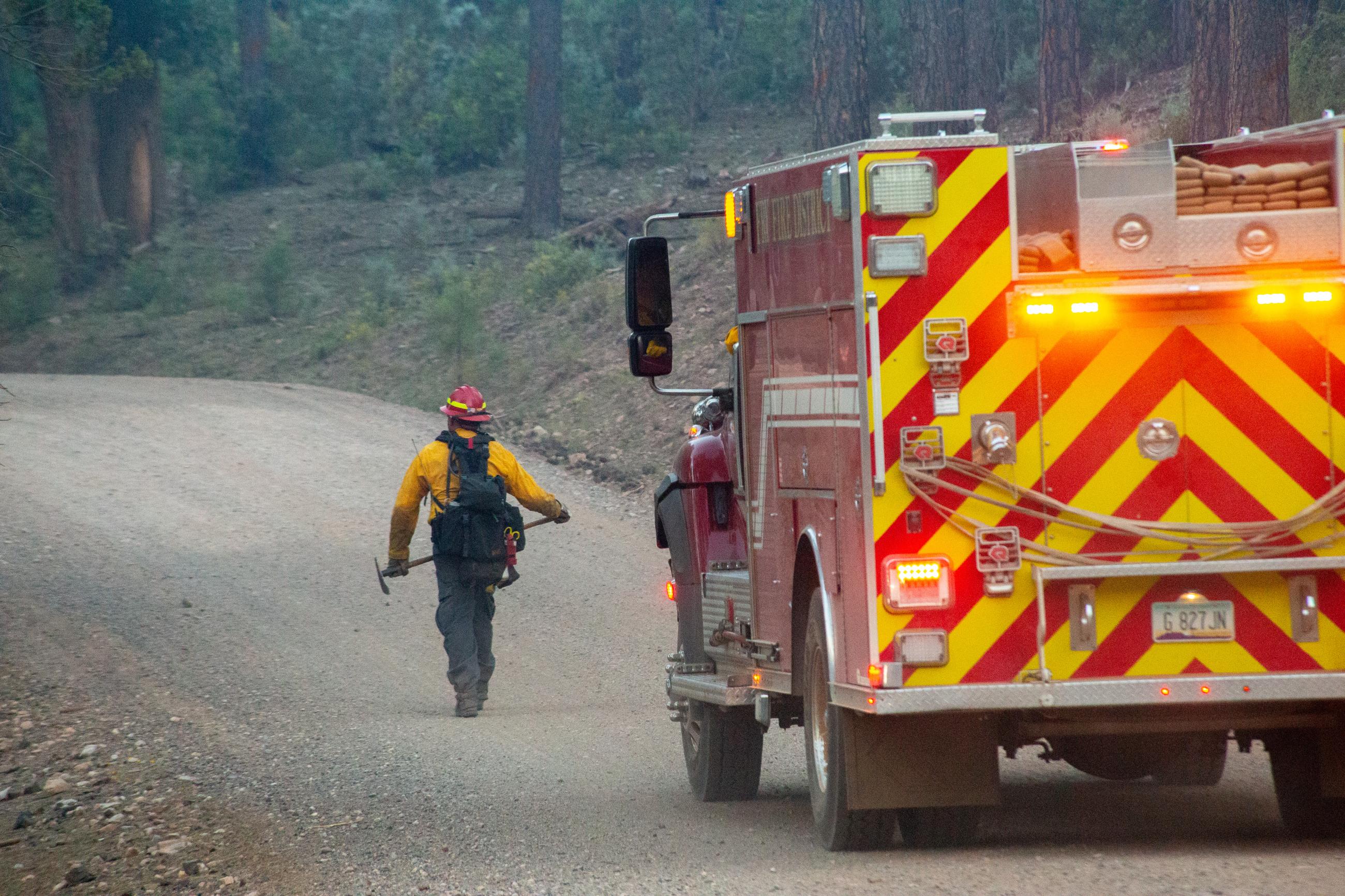 Firetruck with man walking in front of it on a dirt road.