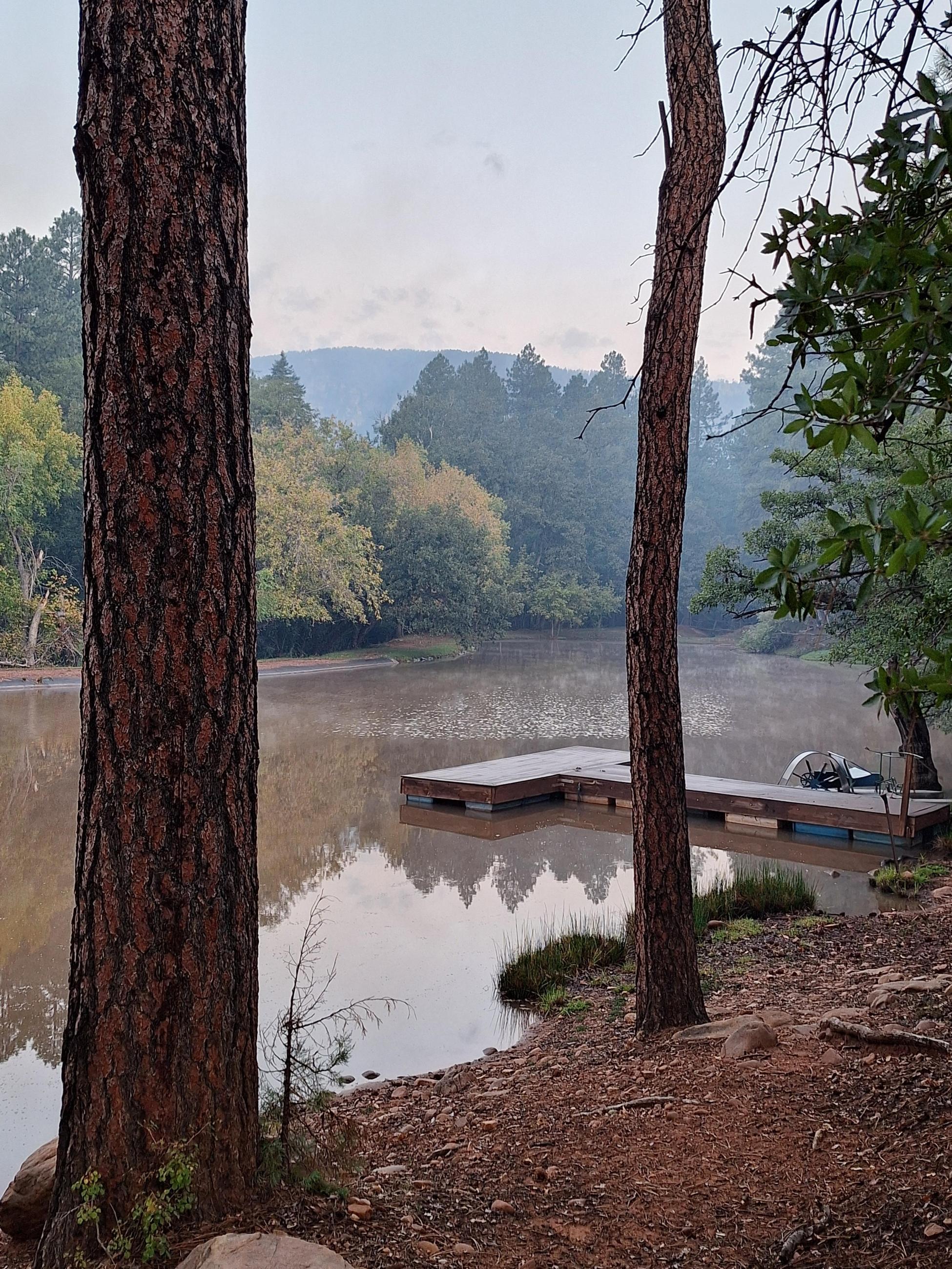 A lake with a dock in the mountains with smoke in the background.