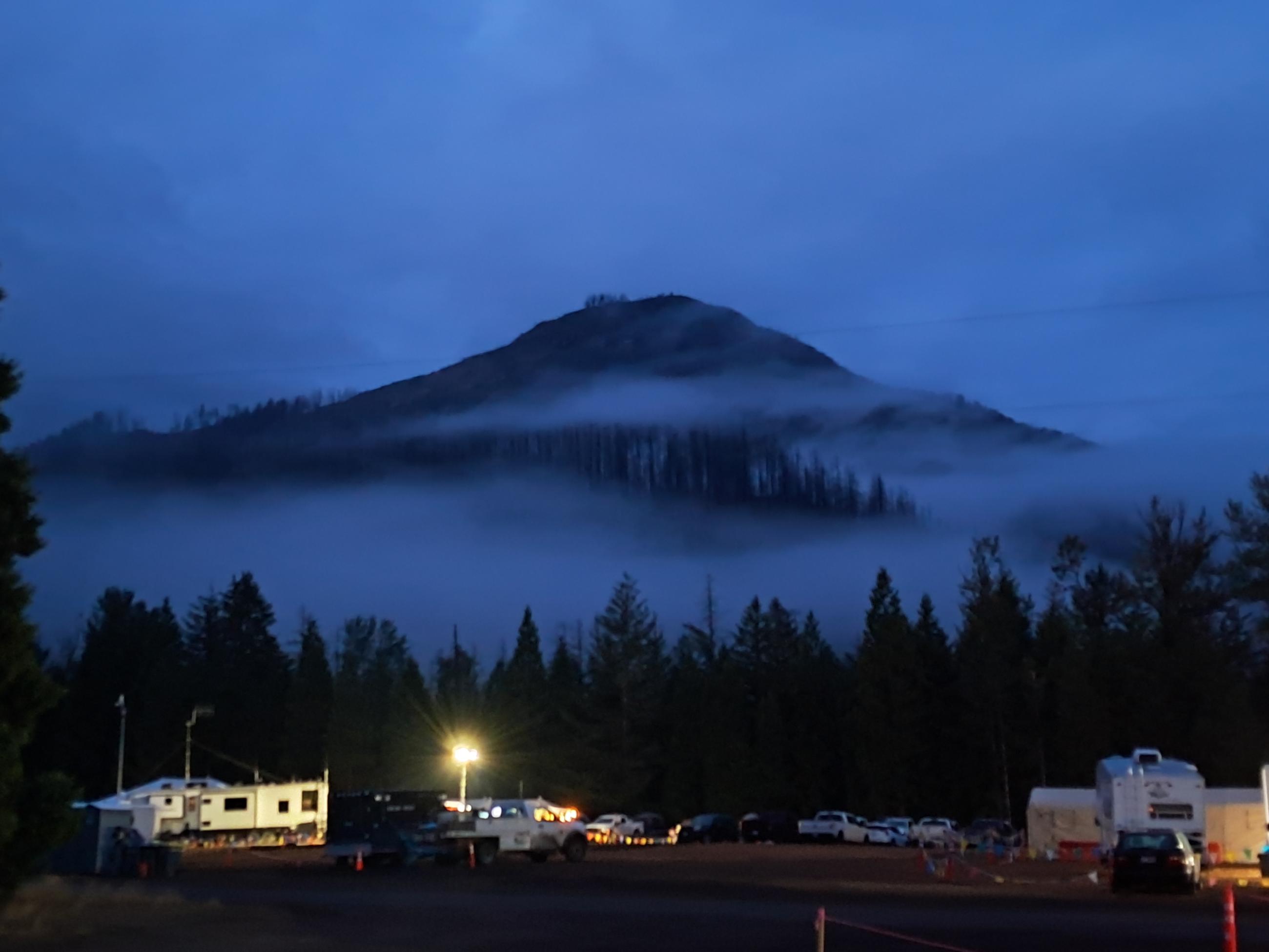 above the fire camp sits a mountain covered in fog.