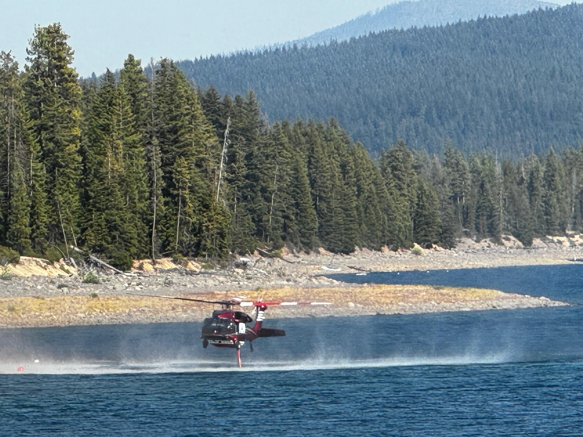 Red helicopter hovering over Crescent Lake and drawing water into it's tank through a snorkel hose