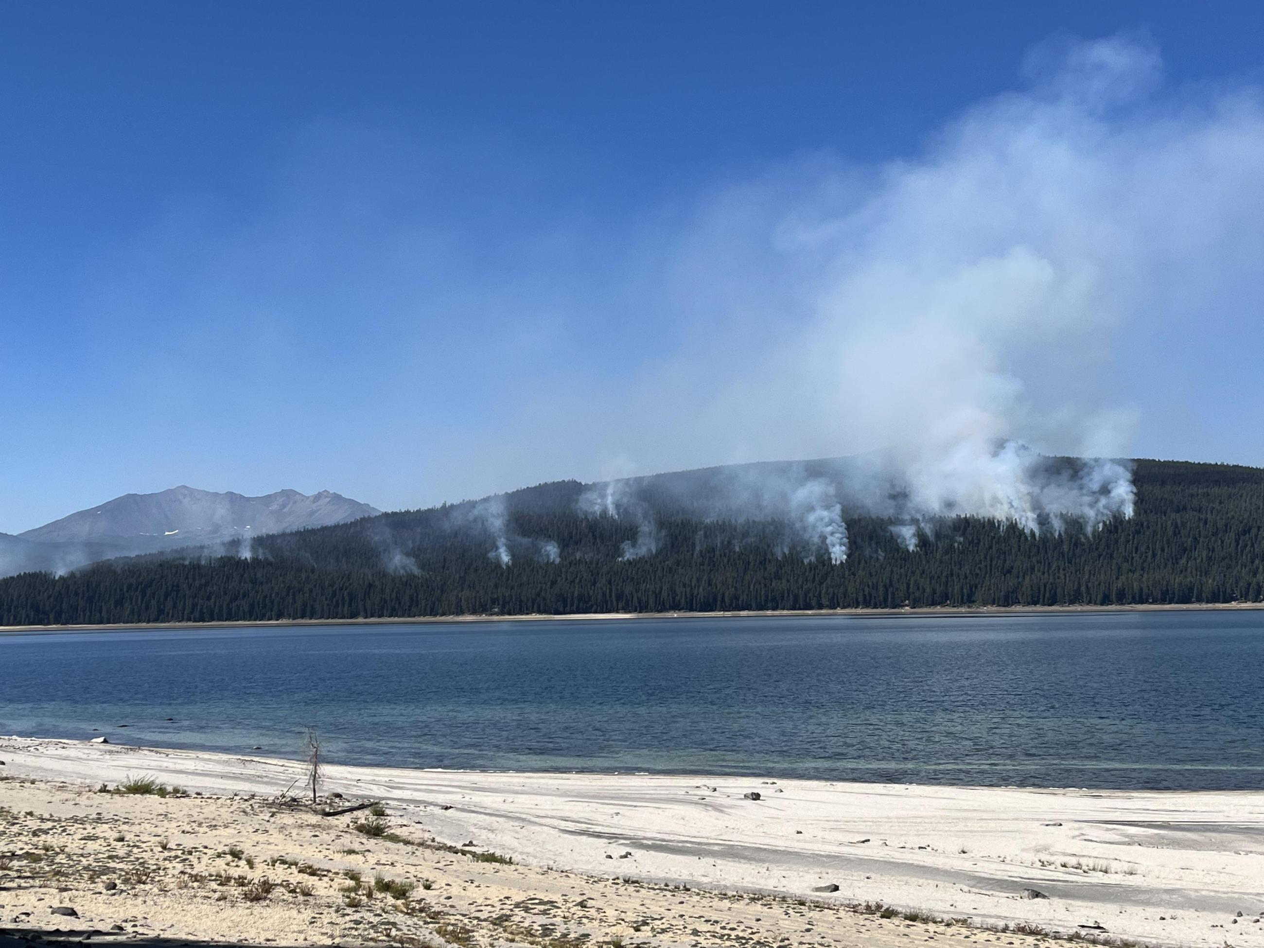 View across Crescent Lake at wispy white smoke rising from the forest from the Red Fire