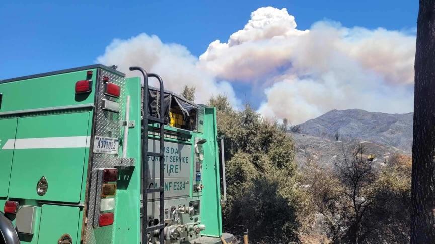 The back of a green California National Forest Brush Patrol Engine parked with a smoke cloud in the distance. 