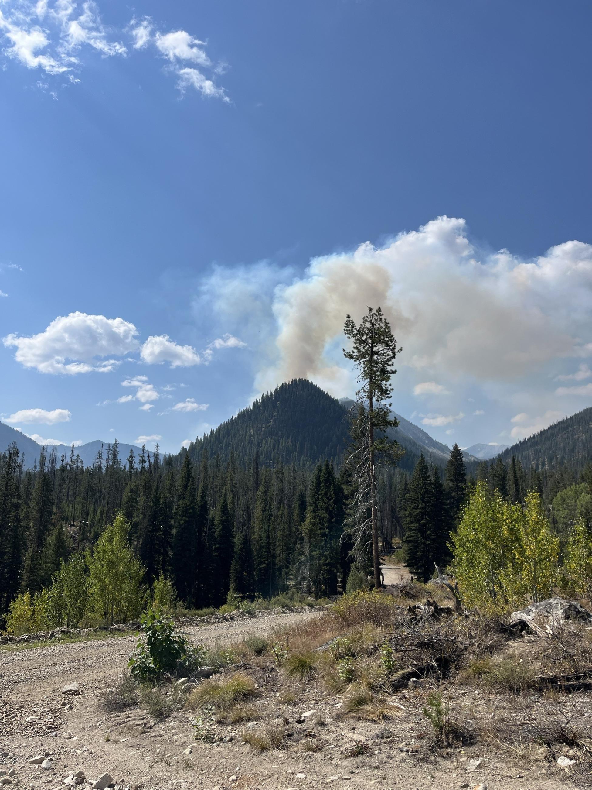 Mountain peak with smoke column rising into a blue sky