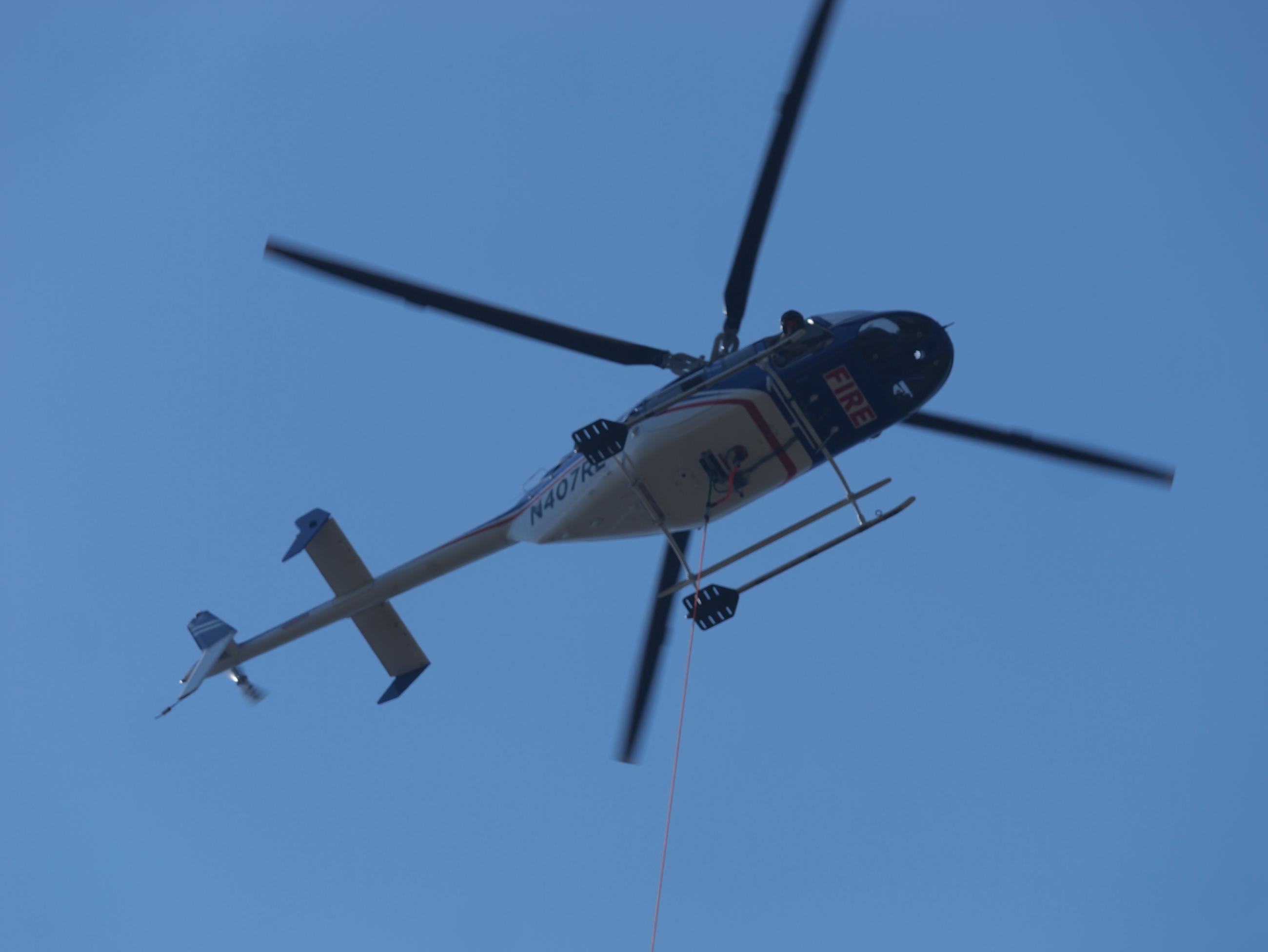 A helicopter with the word "fire" on its belly is seen from below in a clear blue sky.