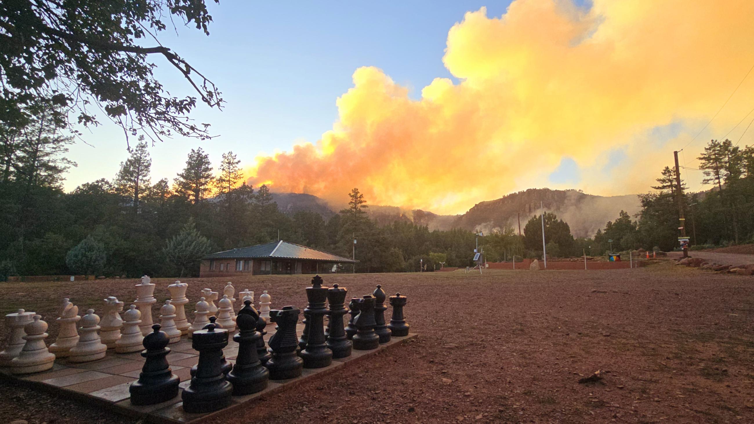 giant chess board with black and white chess pieces in a field with mountains in the background and smoke