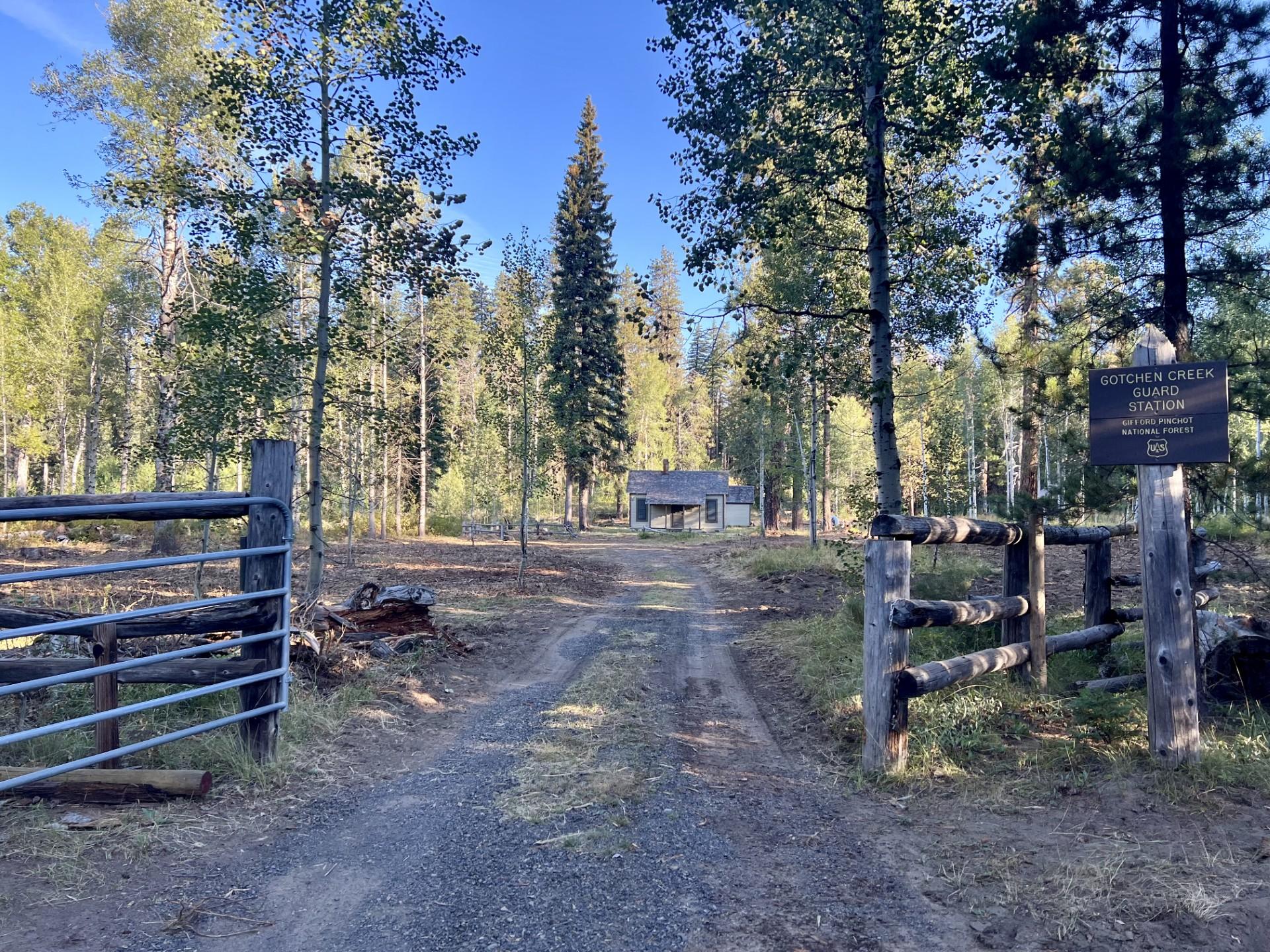 Gotchen Creek Guard Station as seen from the gate, with scattered green trees around the building.