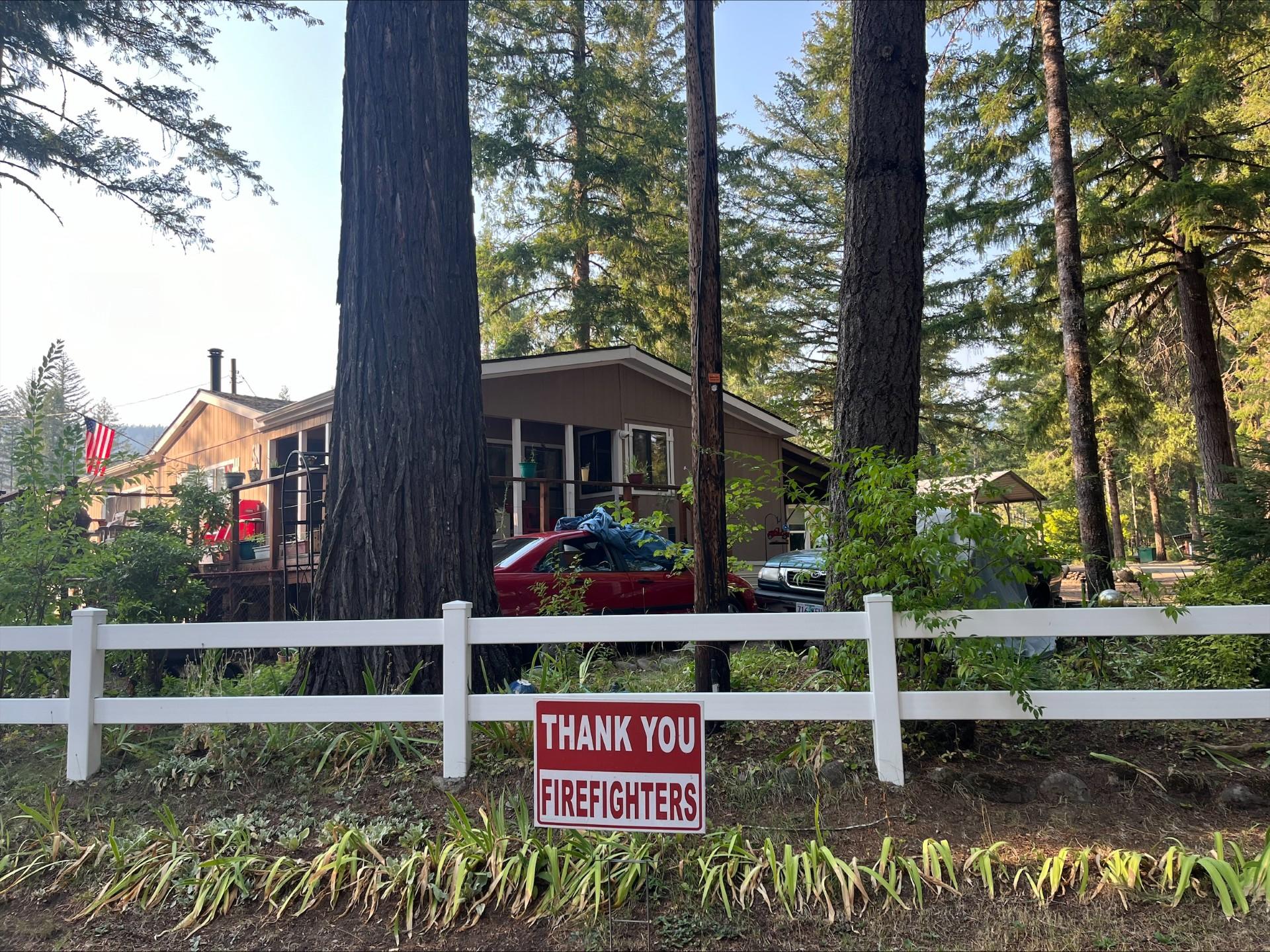 A Thank You Firefighter Sign Hangs from a White Fence.