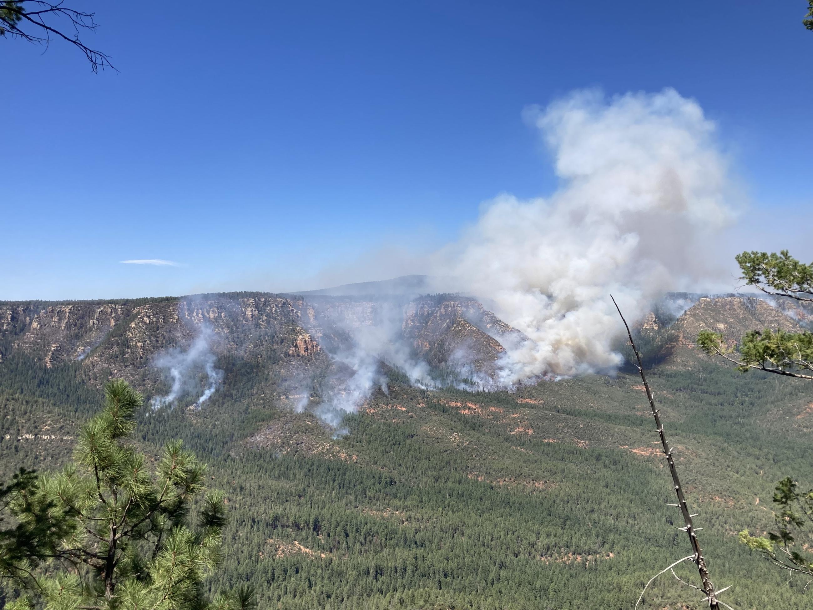 Landscape image of a valley with steep terrain and smoke in the background.