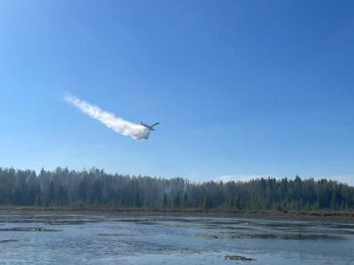 An airplane drops water over a forest by a lake. 