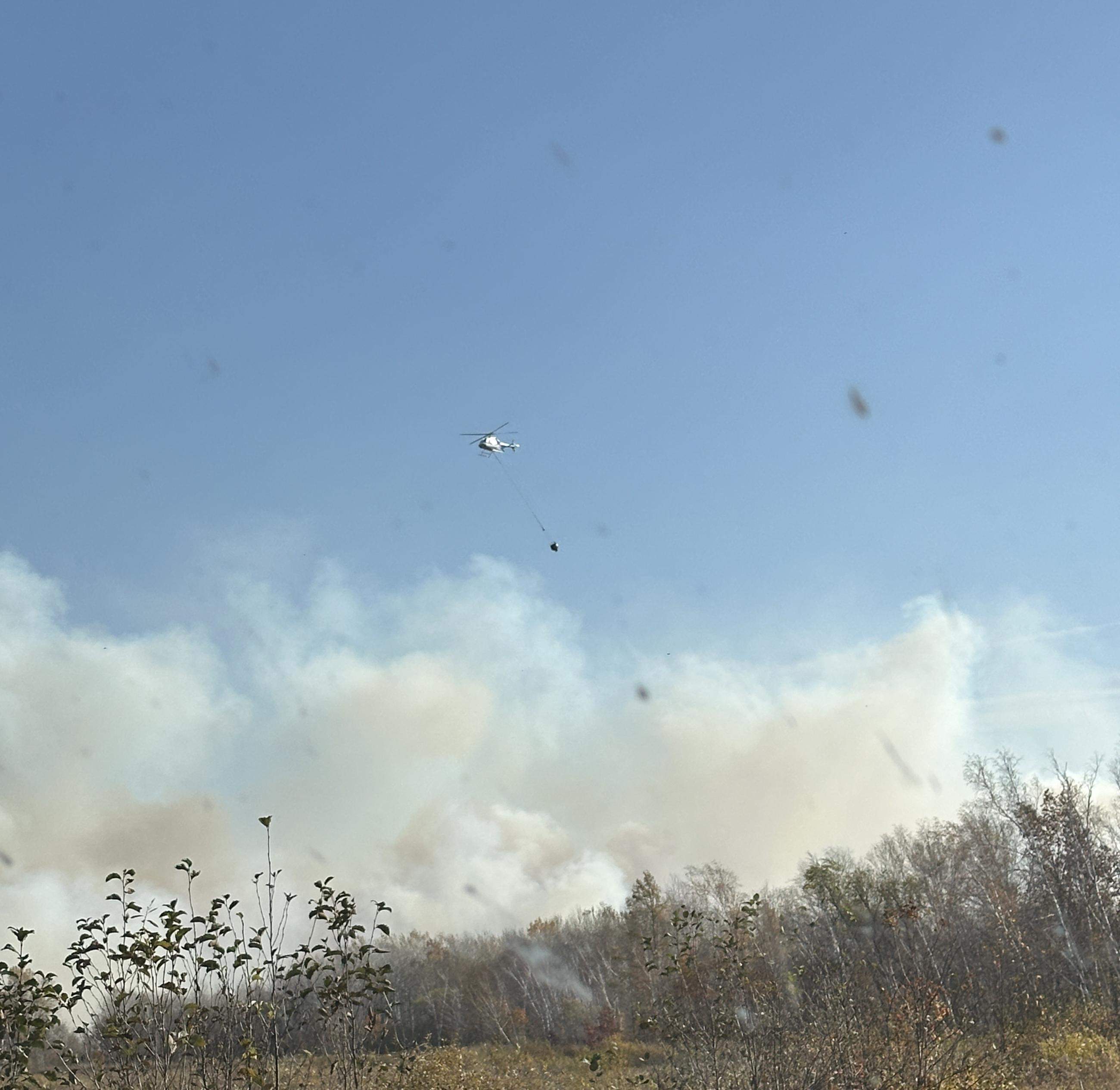 A helicopter with a bucket flies over wildfire