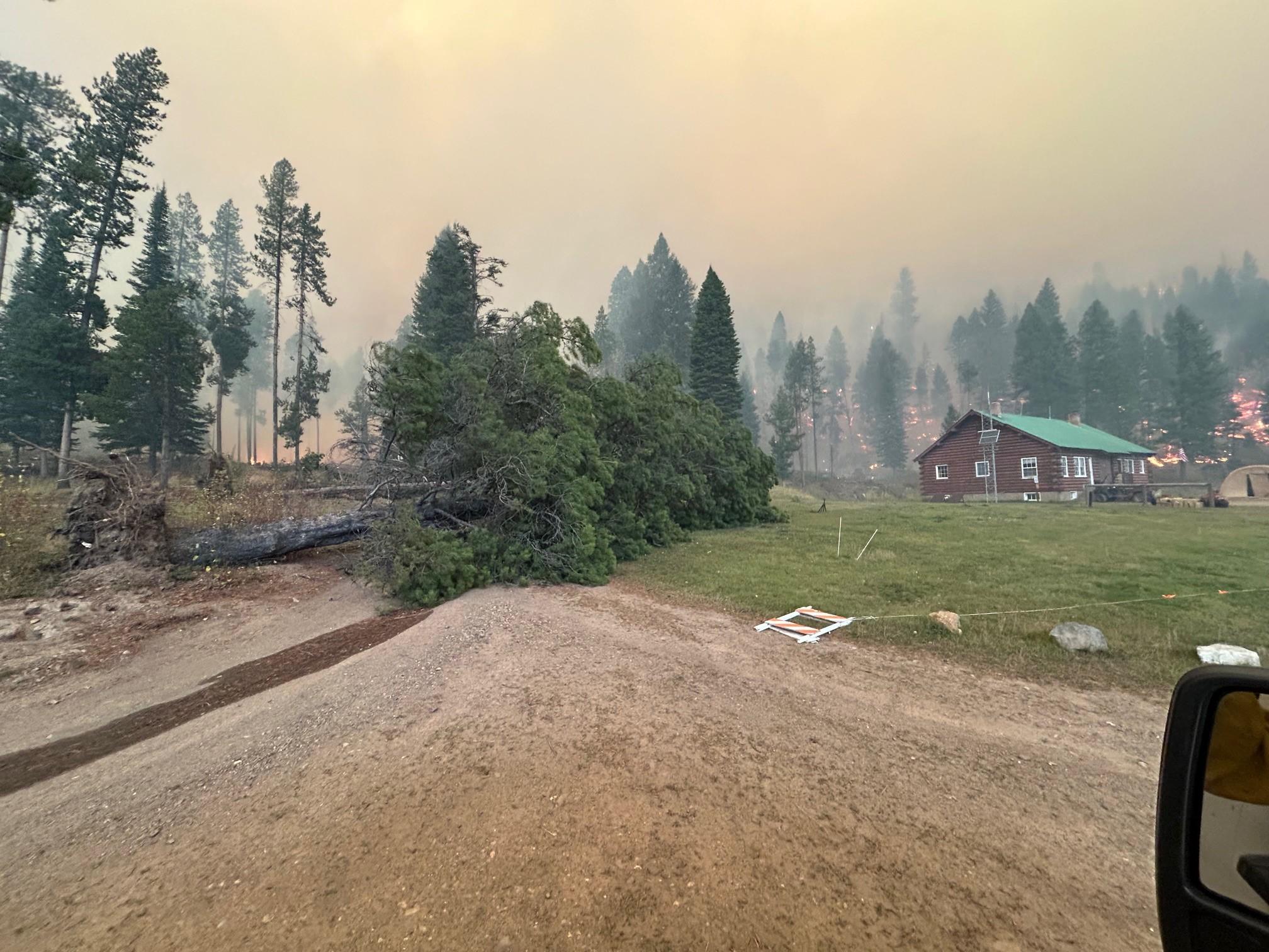 Photo shows the Forest Service Big Creek Guard Station with fire behind it.