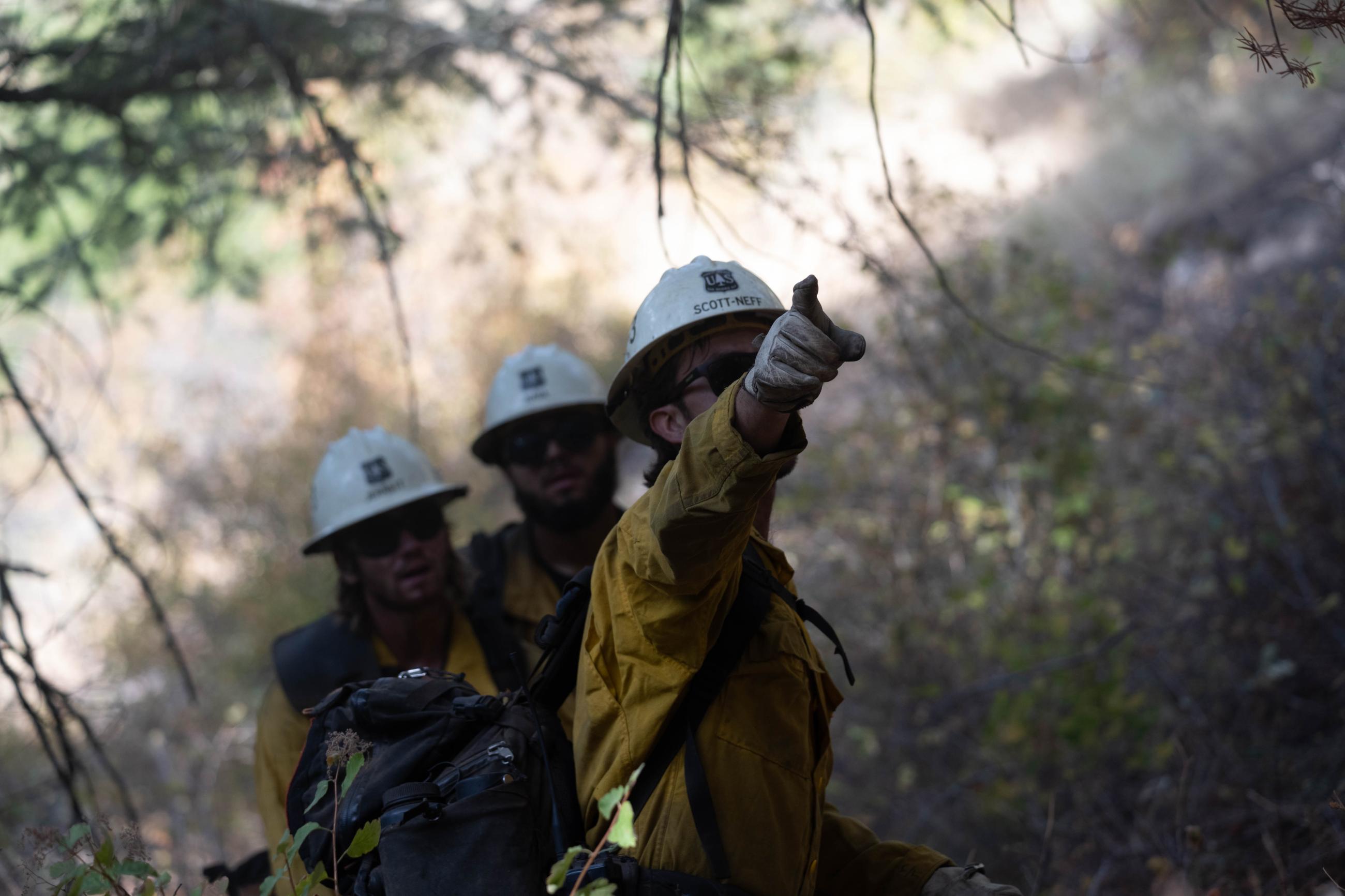 Three firefighters stand in a row while one points uphill