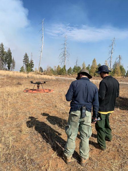 Two firefighters prepare to launch a drone for UAS Operations with a smoke plume in the background