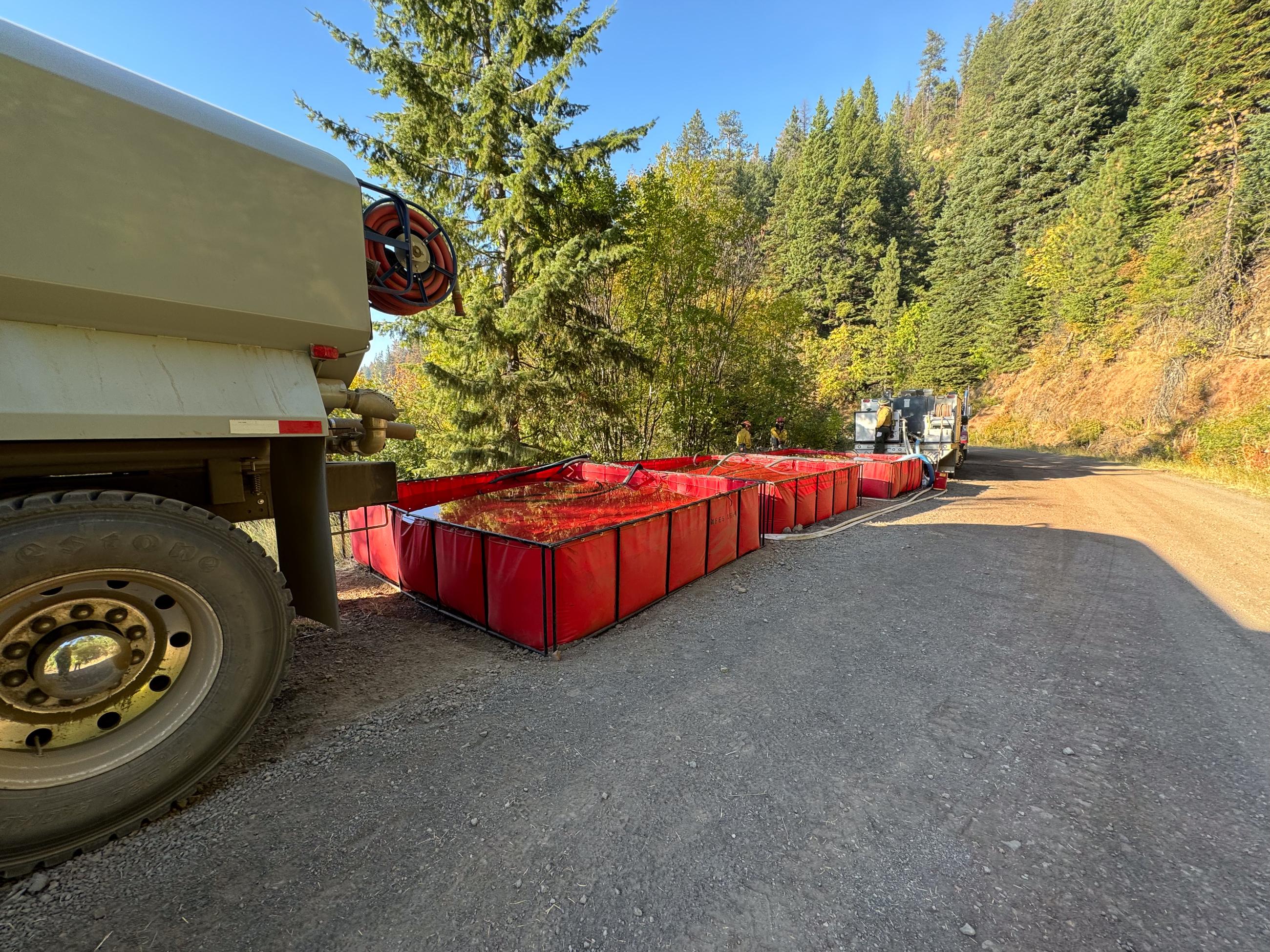 line of red tanks connected by firehoses with trucks at front and back