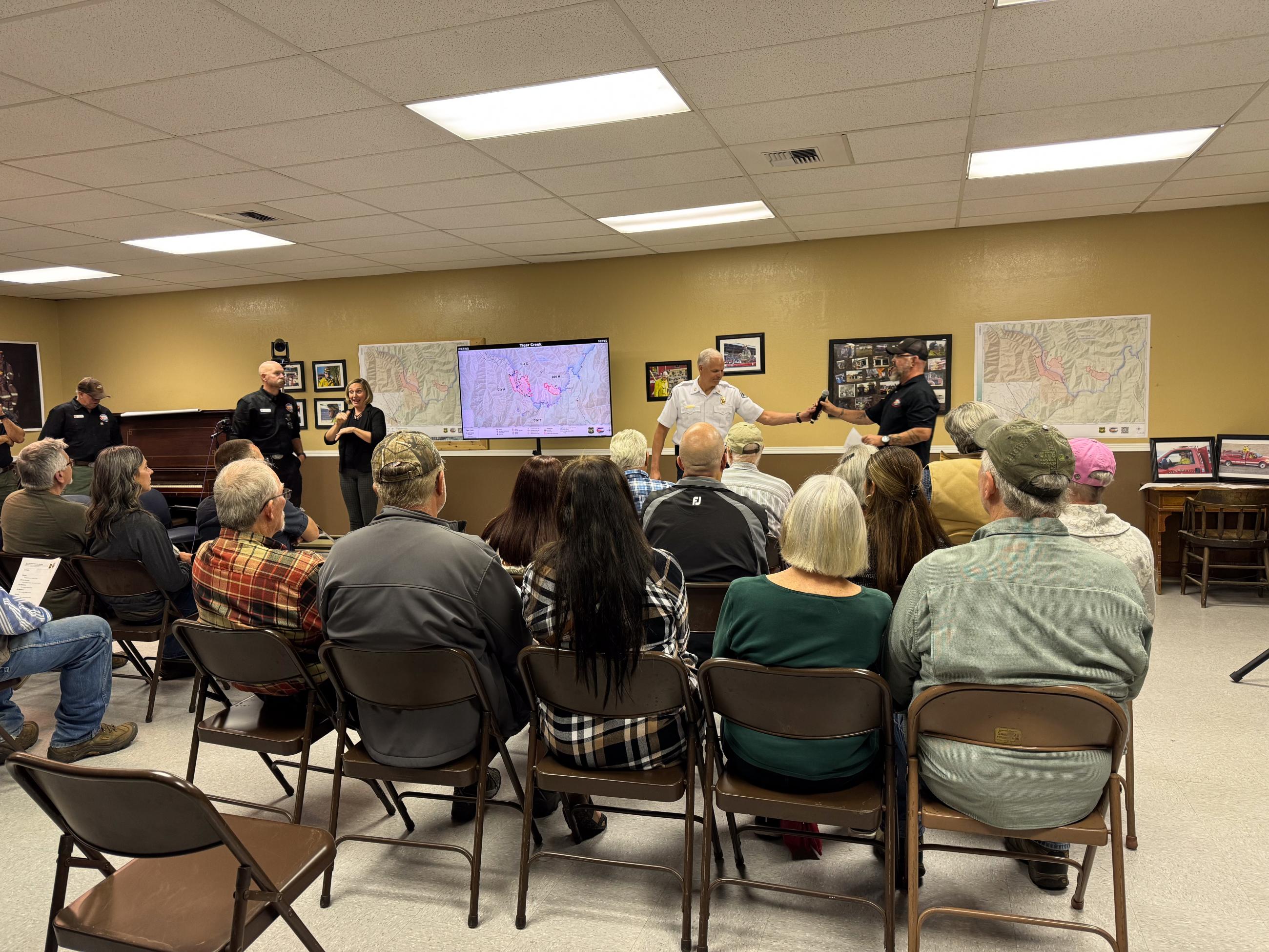 Large group of people sitting facing front with large maps on the wall.