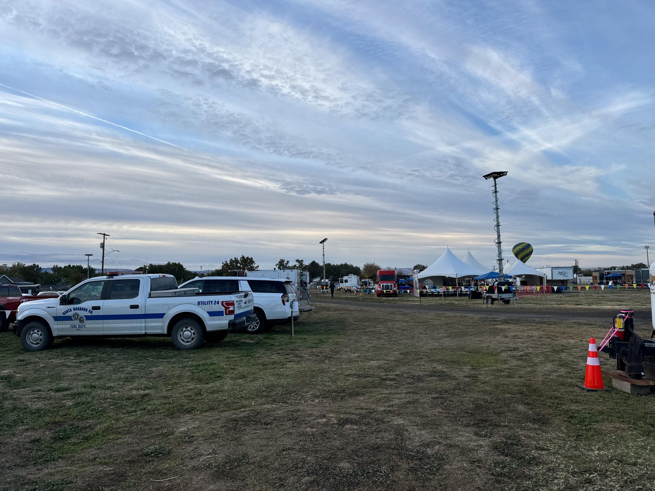 vehicles in foreground, large tents with a hot air balloon rising up the camp