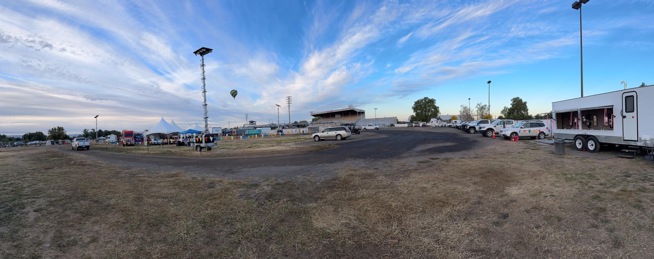 Hot Air balloon in the middle of the view with many vehicles and trailers spread underneath at camp