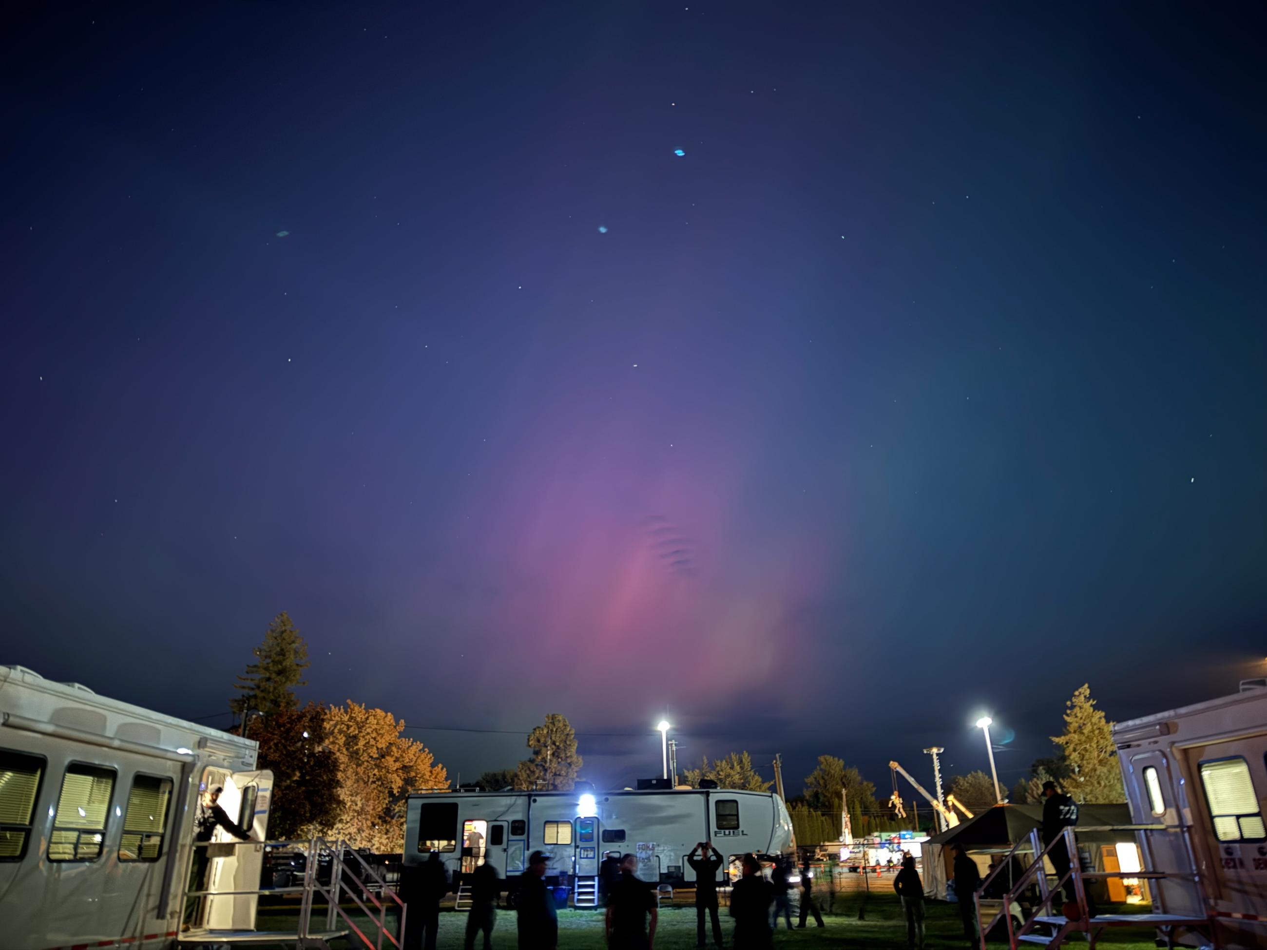 Large pink aurora in dark sky with trailers lit on ground.