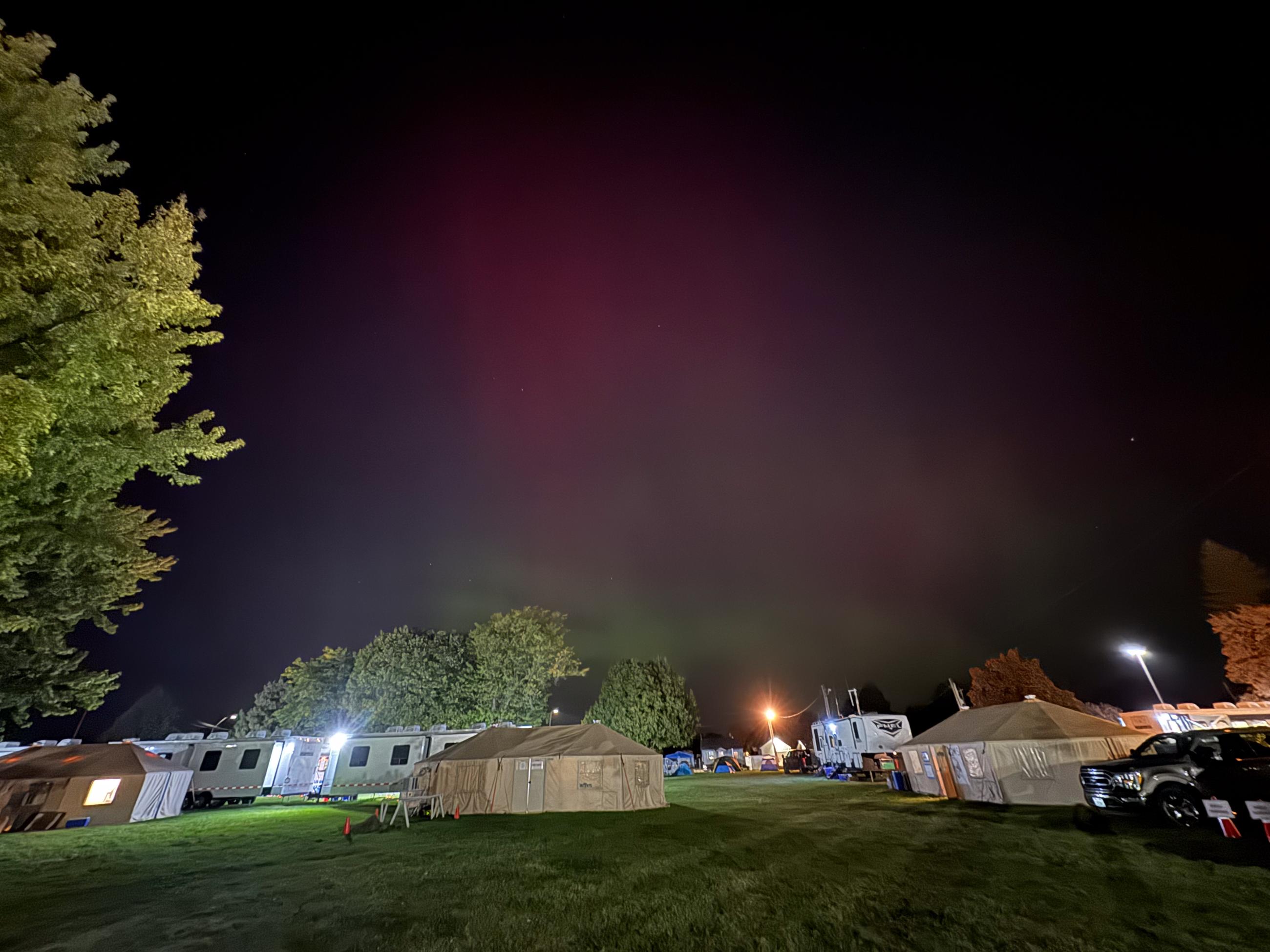 Dark sky with pink aurora in center of photo with tents and trailers underneath.