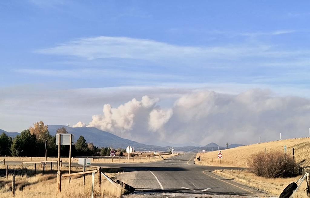 large smoke column coming off the top of a mountain and drifting to the right with a highway in the foreground