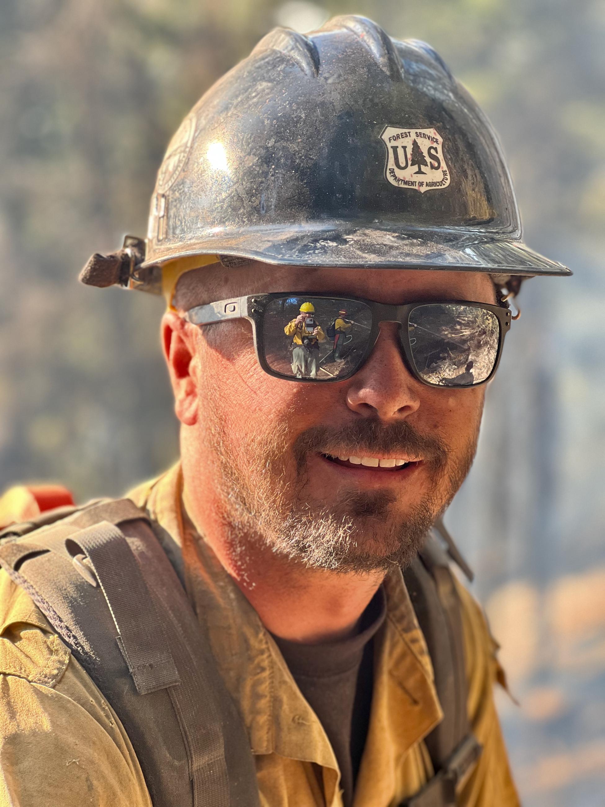 A firefighter wearing a black helmet with a US Forest Service insignia is seen in a portrait taken on the Goat Fire.