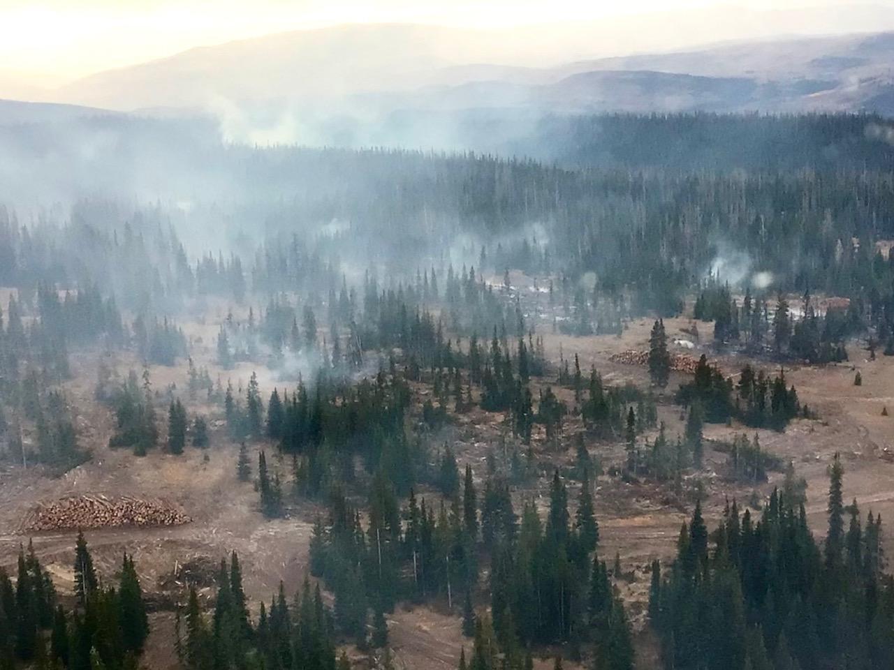 Log deck in the left side of frame with smoke in the sky and pine trees dotting the landscape.