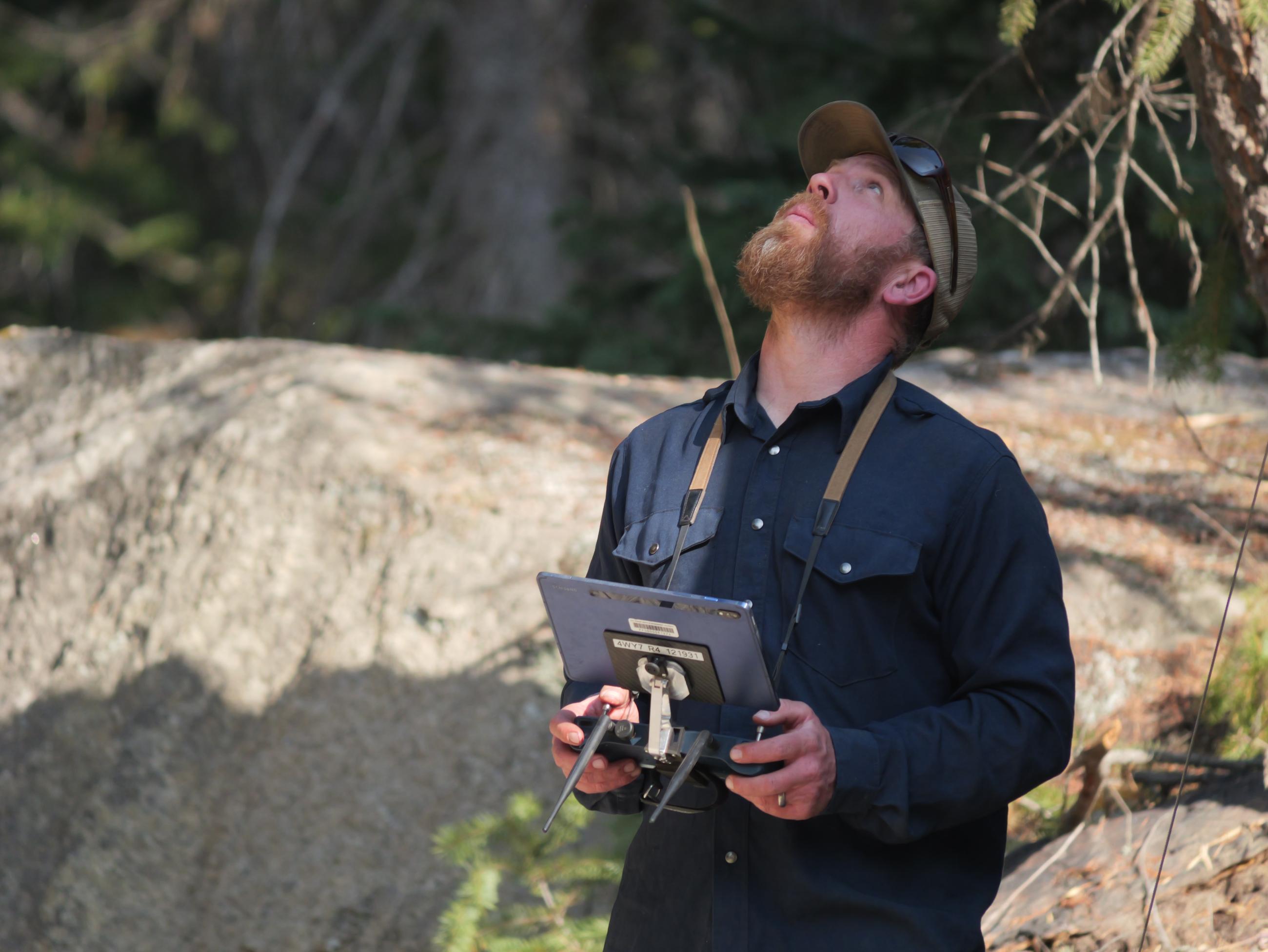 A firefighter holding an electronic tablet uses the tablet to pilot a drone.