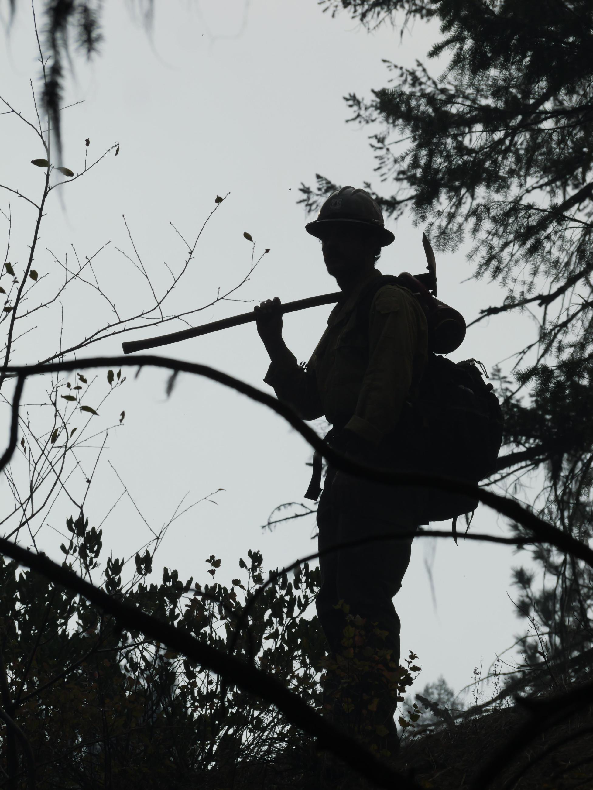 A firefighter with a tool over his shoulder is seen in silhouette. 